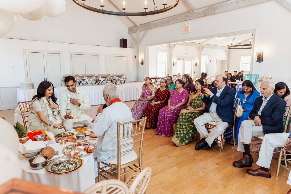 Traditional Indian wedding ceremony gathering in a bright white event space with guests seated.