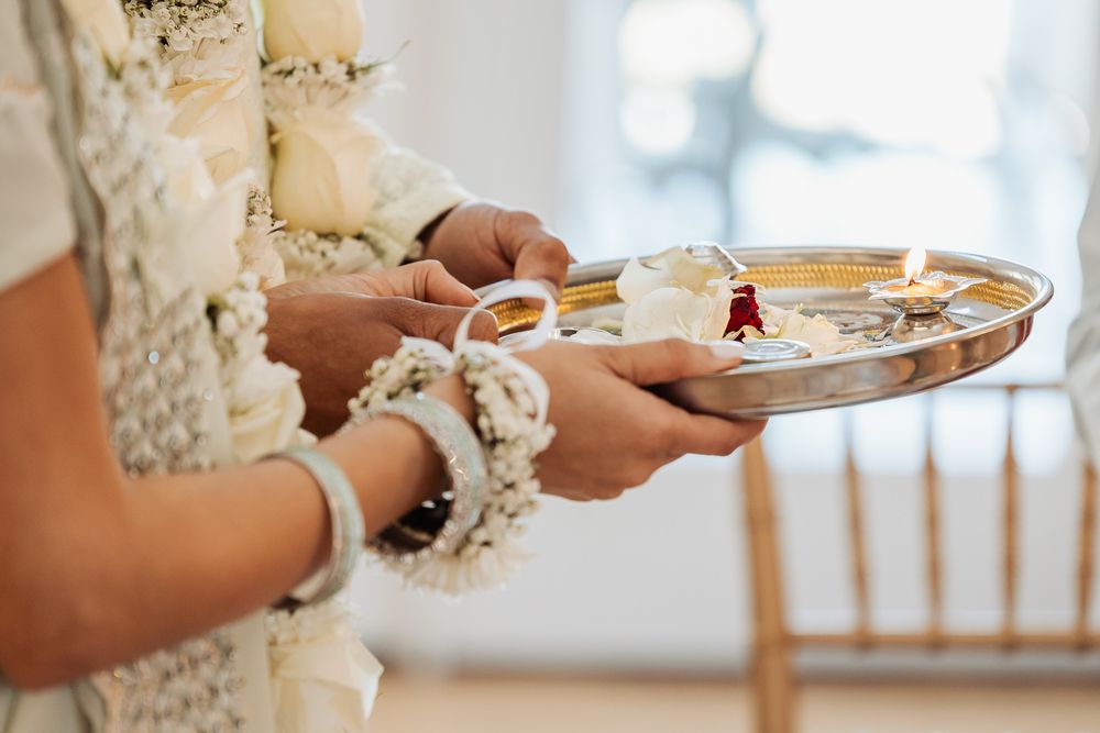 Close-up of hands holding decorative silver plate with traditional Indian wedding items.