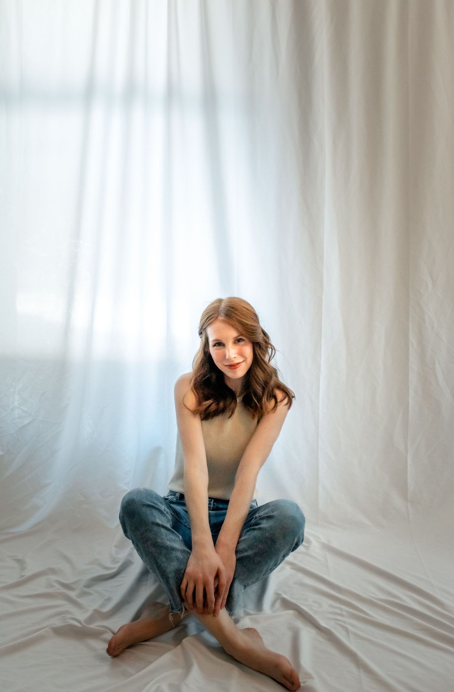 Stylish casual portrait against white backdrop with beige turtleneck and blue jeans creating minimalist aesthetic.