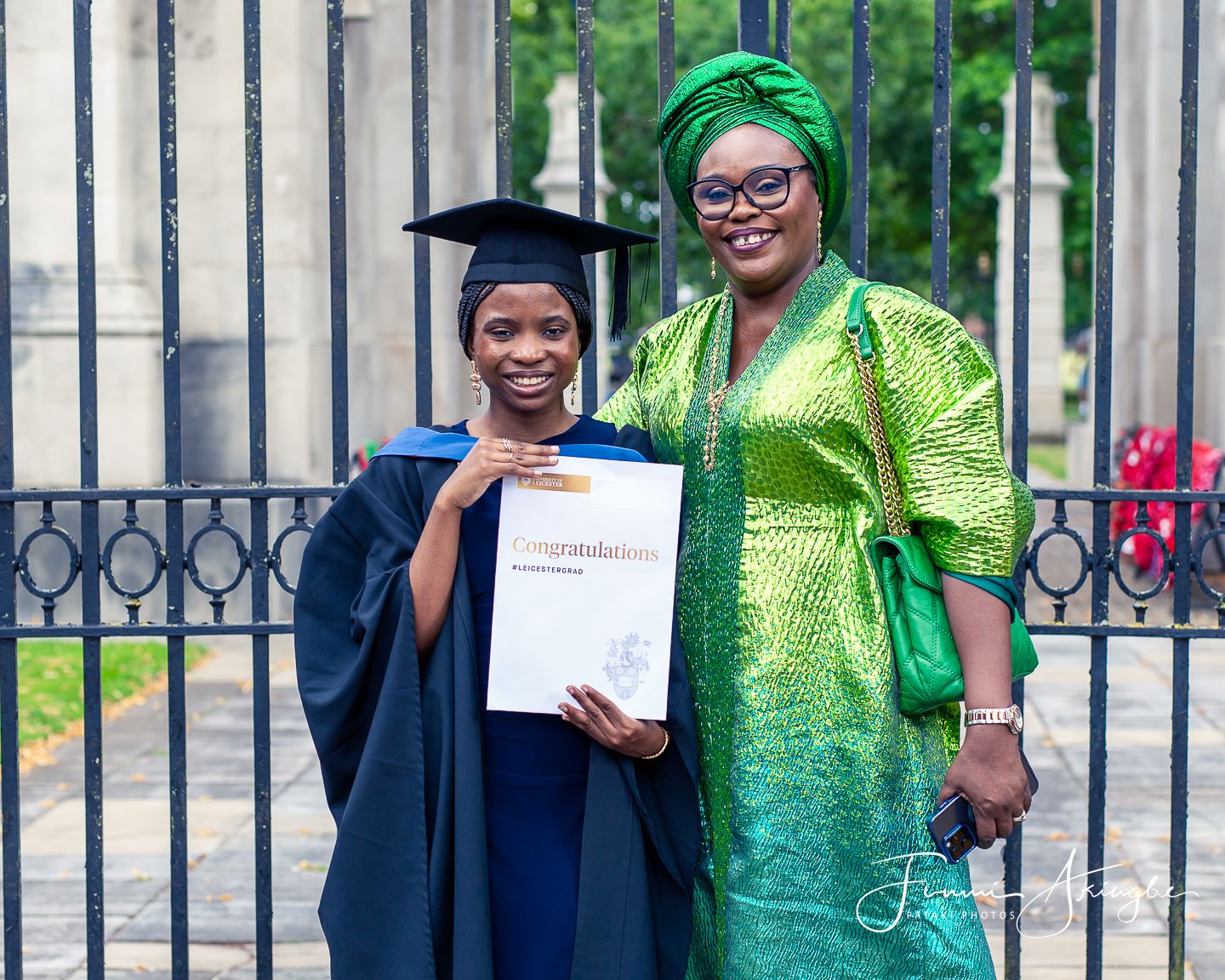 A graduate in cap and gown proudly displays her diploma while posing with her mother