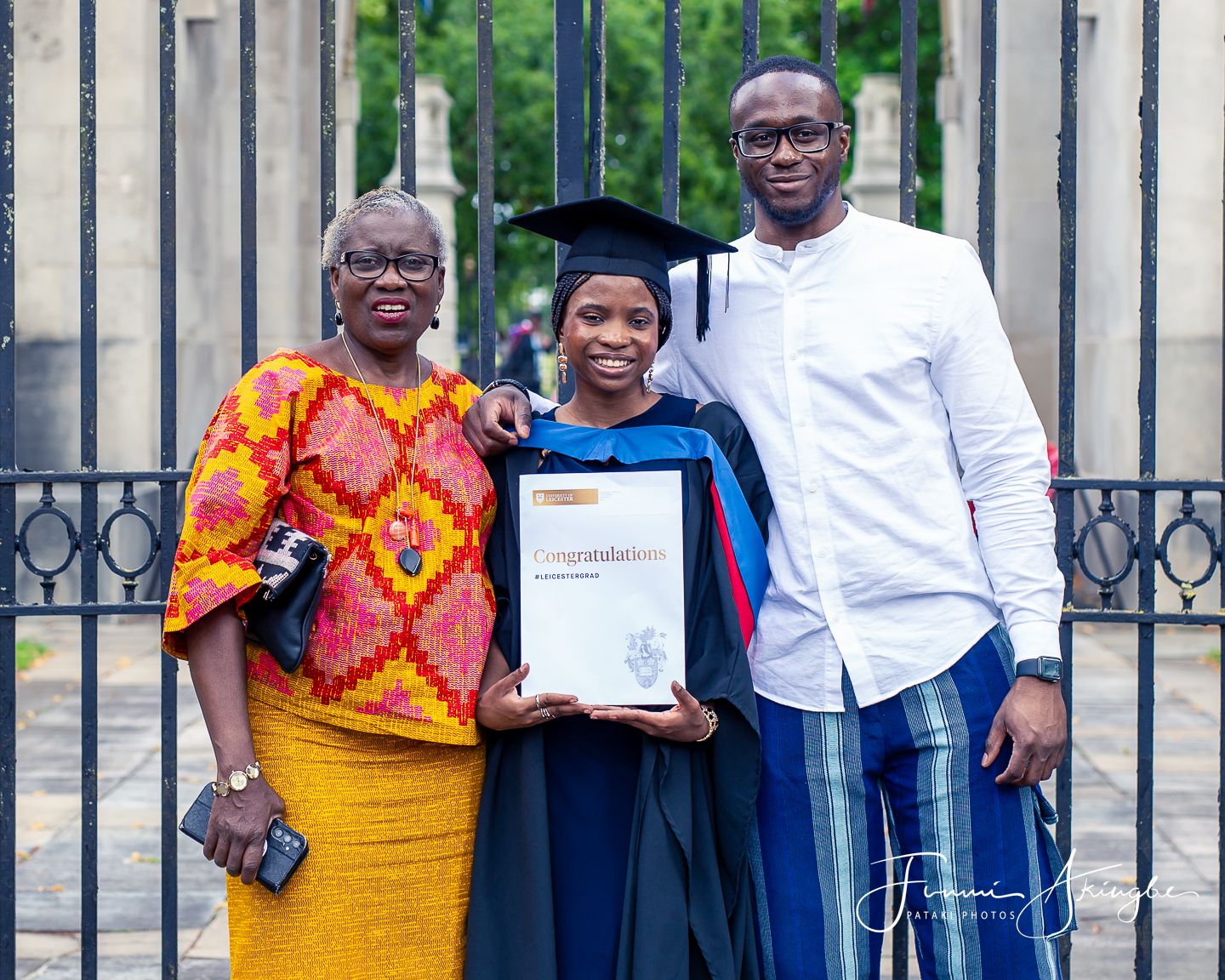 A graduate in cap and gown proudly displays her diploma while posing with her brother and aunty
