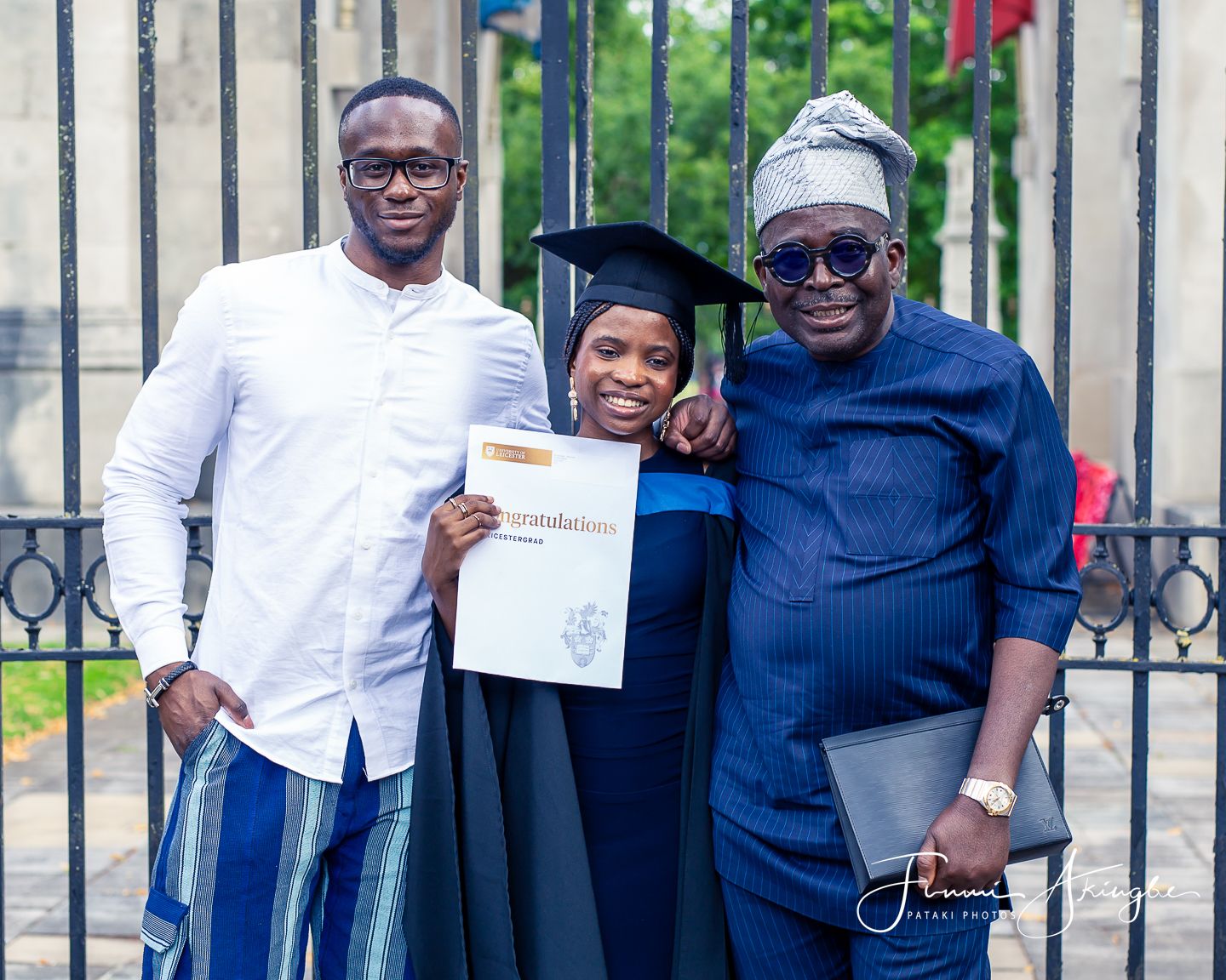 A graduate in cap and gown proudly displays her diploma while posing with her brother and uncle