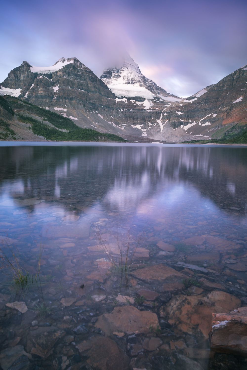 Snow-capped mountain peaks reflecting in crystal clear alpine lake waters at dusk.