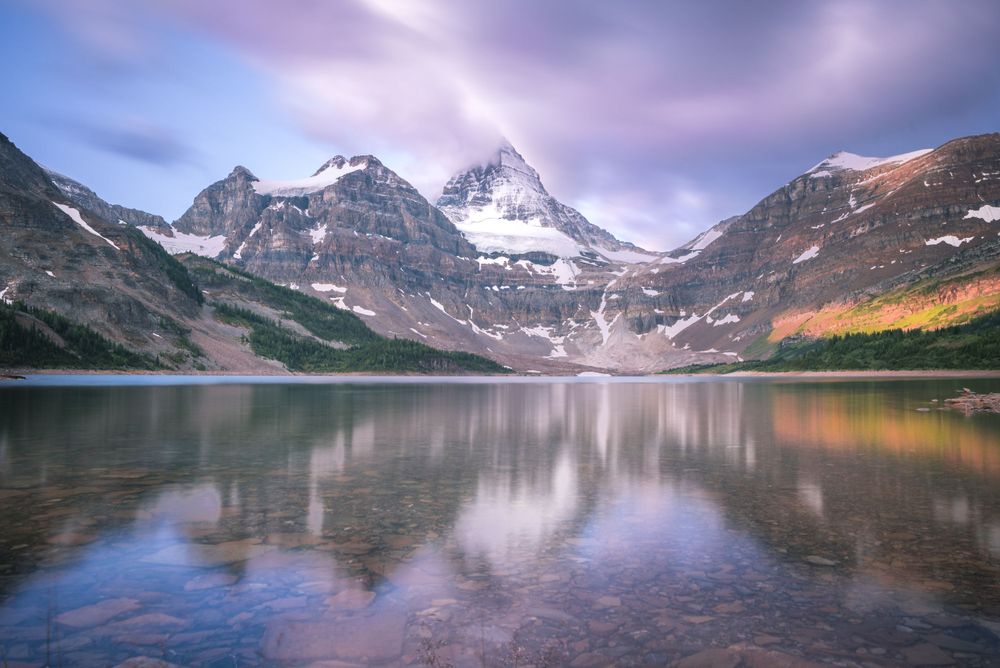 Majestic mountain landscape reflected in calm lake waters during sunset with purple sky.