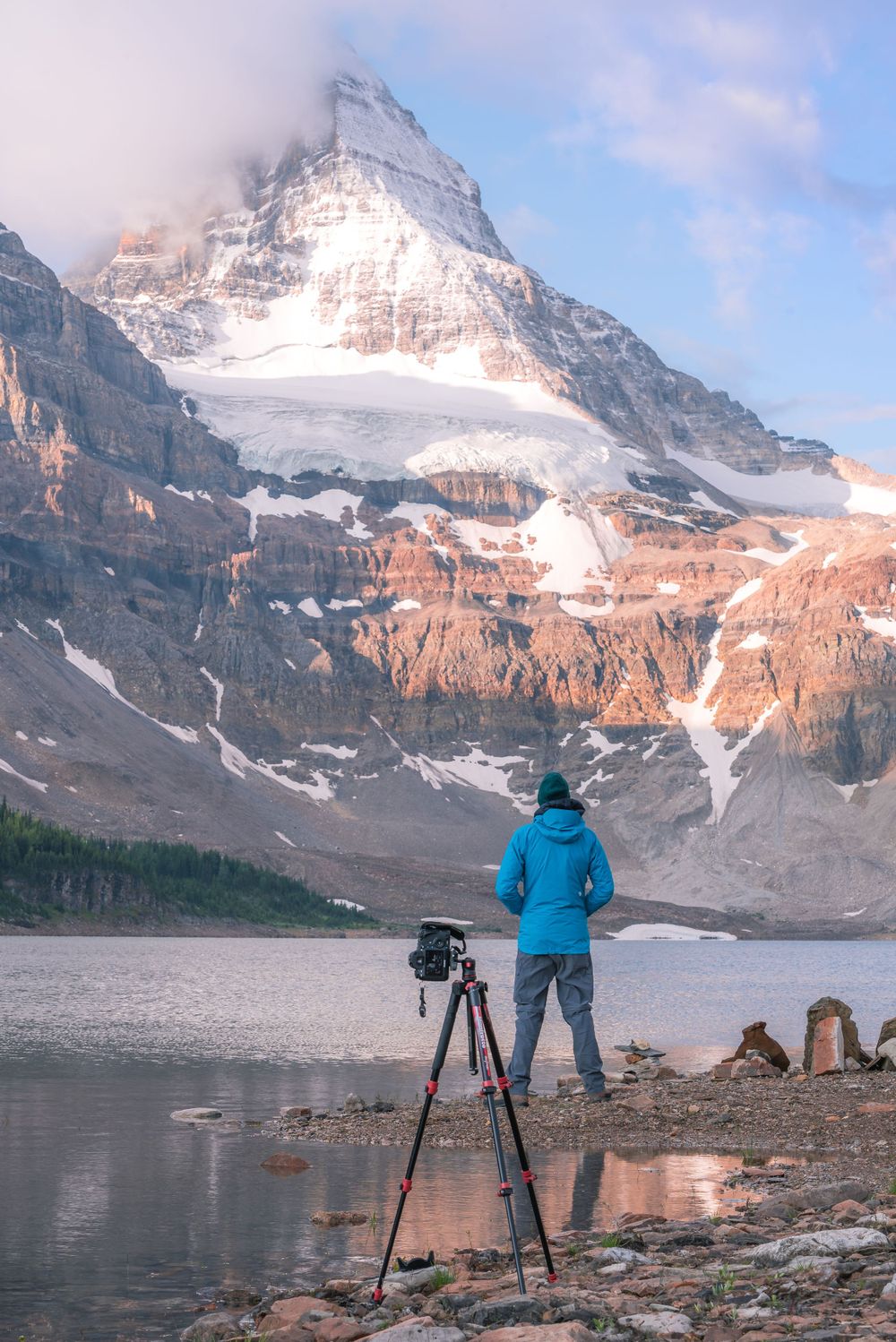 Photographer with tripod capturing mountain scenery beside an alpine lake.