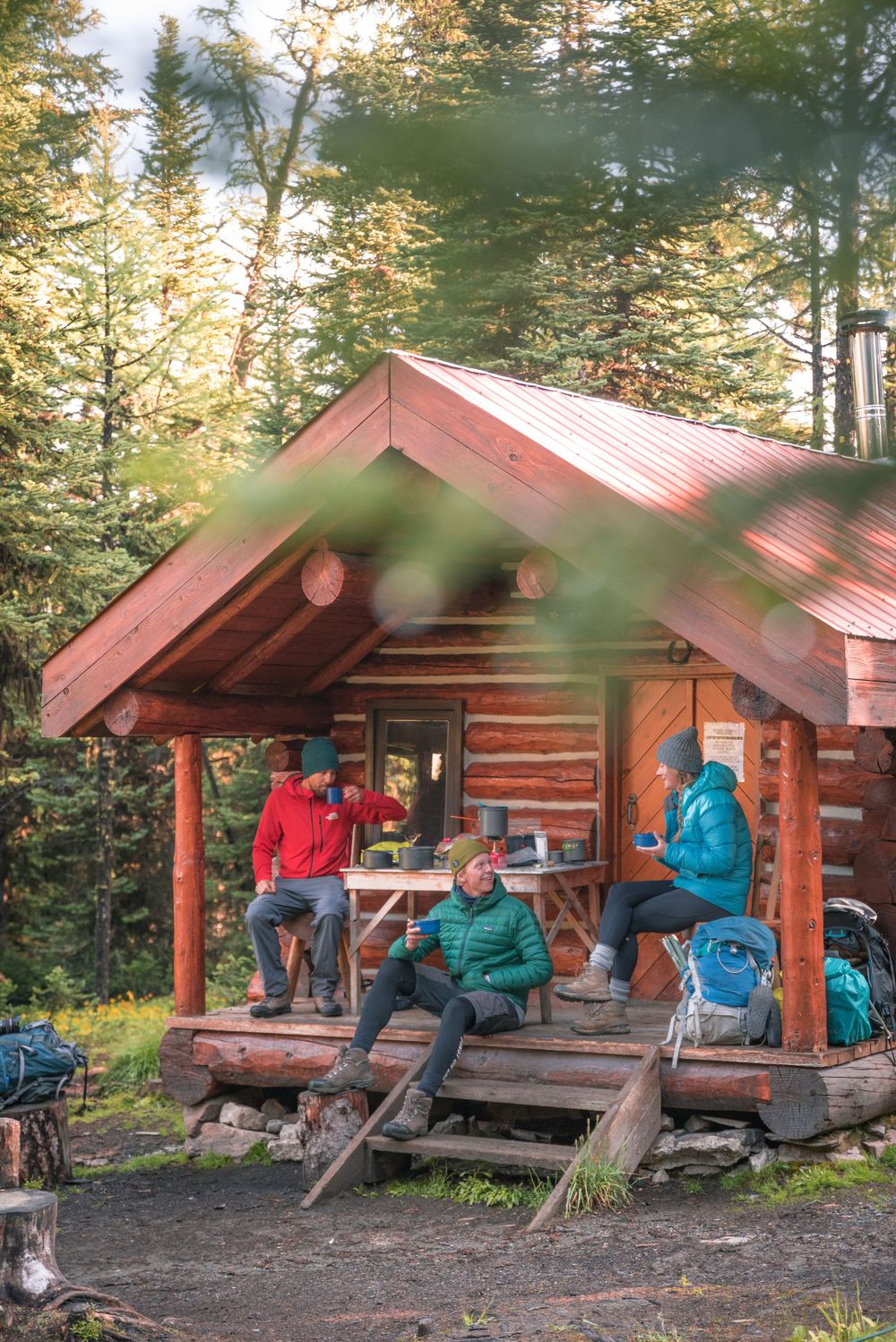 Hikers resting at a rustic log cabin shelter in a forested mountain setting.