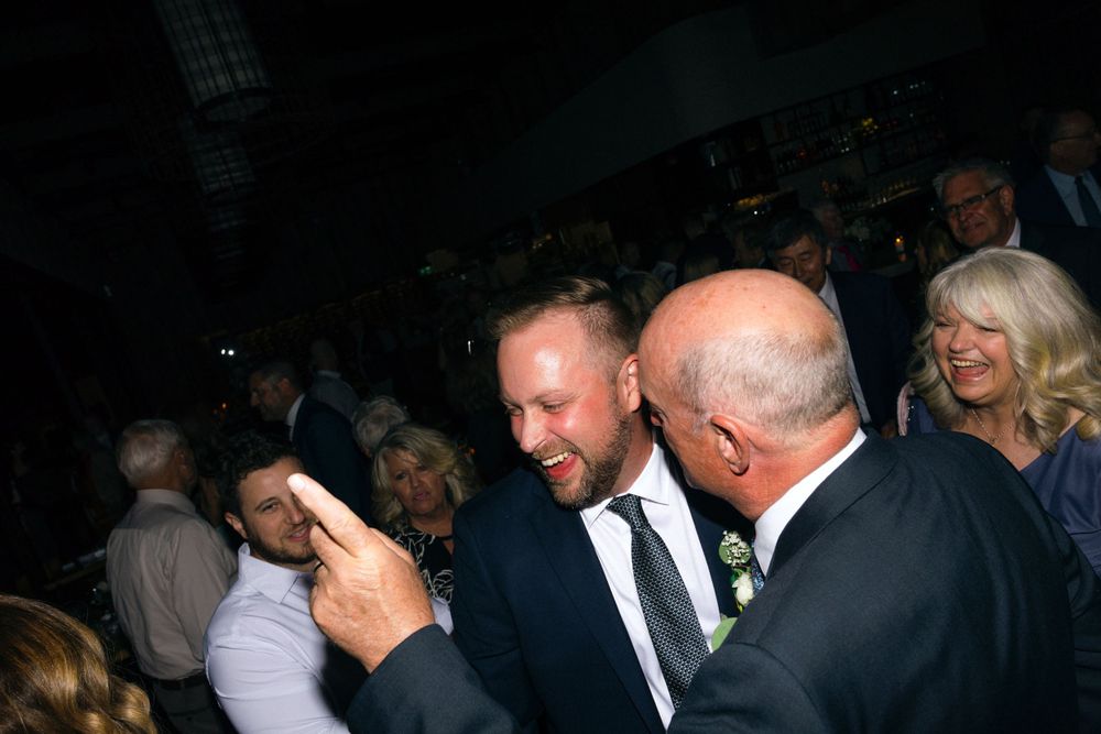 People celebrate and socialize together at a dimly lit event, with laughter and smiles visible in the crowd.