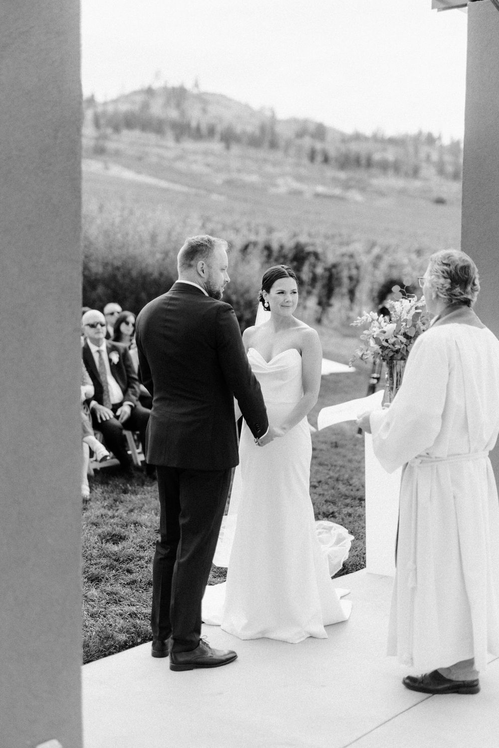 A black and white outdoor wedding ceremony with guests seated and a beautiful mountain landscape in the background in the Okanagan