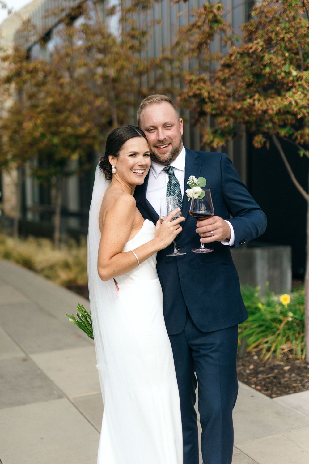 A couple in wedding attire shares a celebratory toast while standing outdoors.
