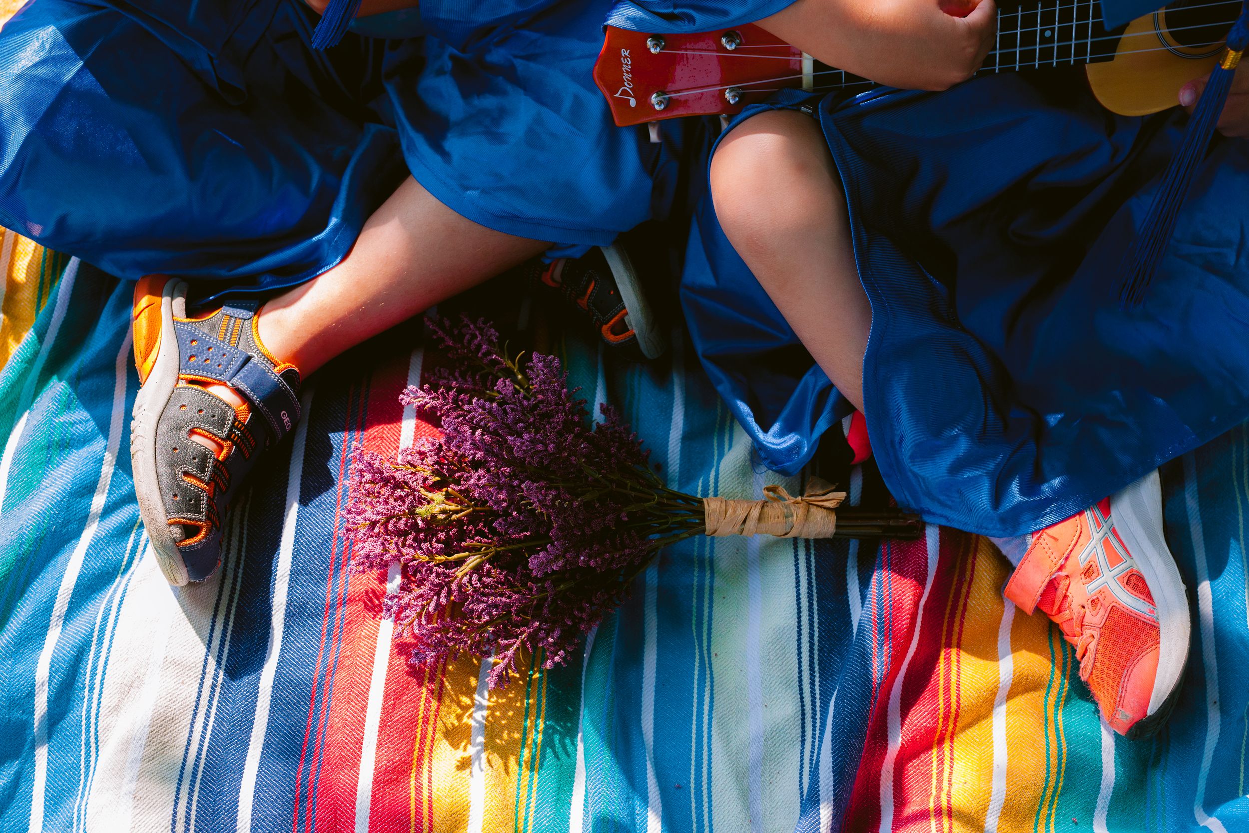 Someone in blue denim and red sneakers relaxes on a striped blanket with pink flowers and a guitar.