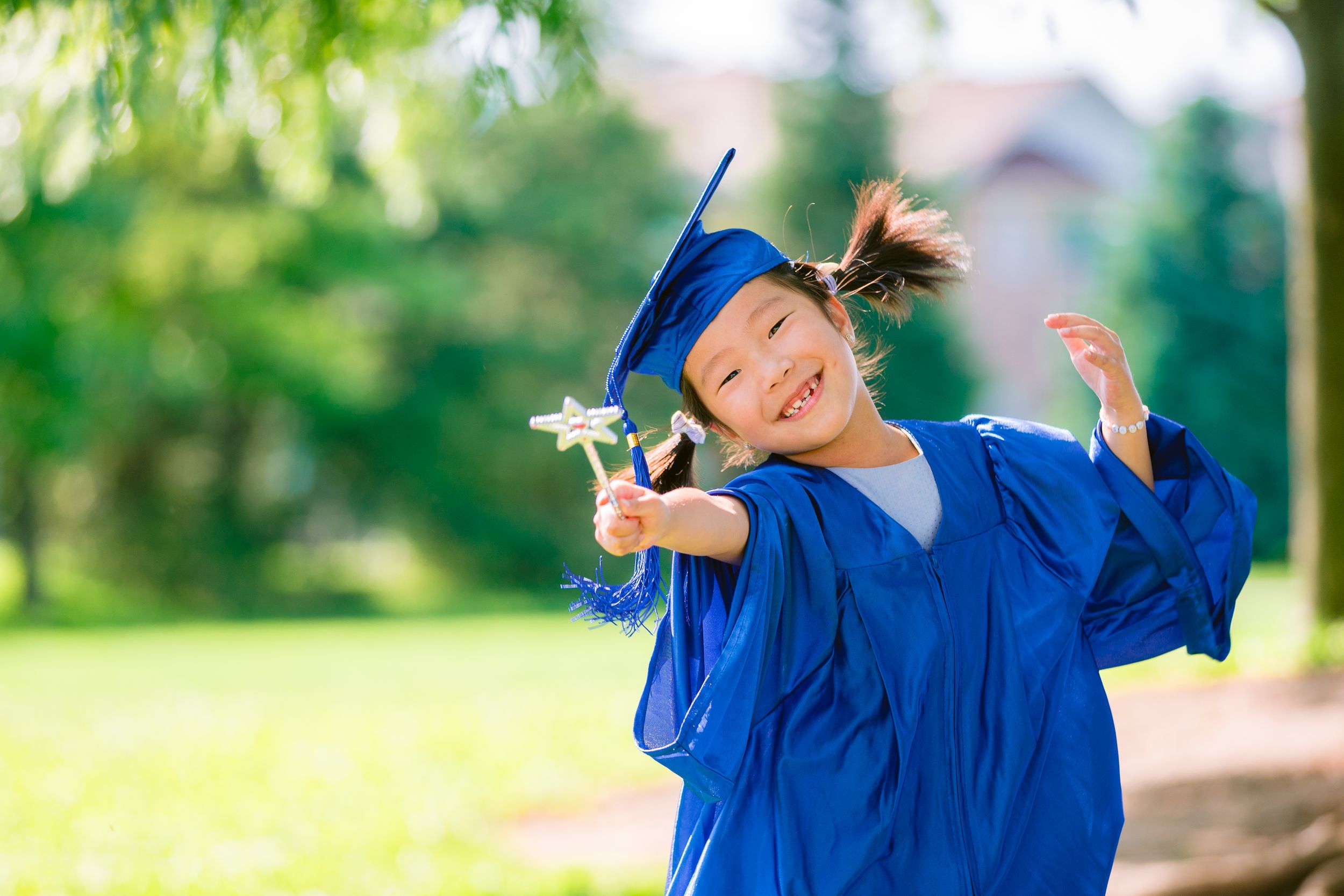Graduate in bright blue cap and gown holds diploma while joyfully celebrating outdoors on a sunny day.