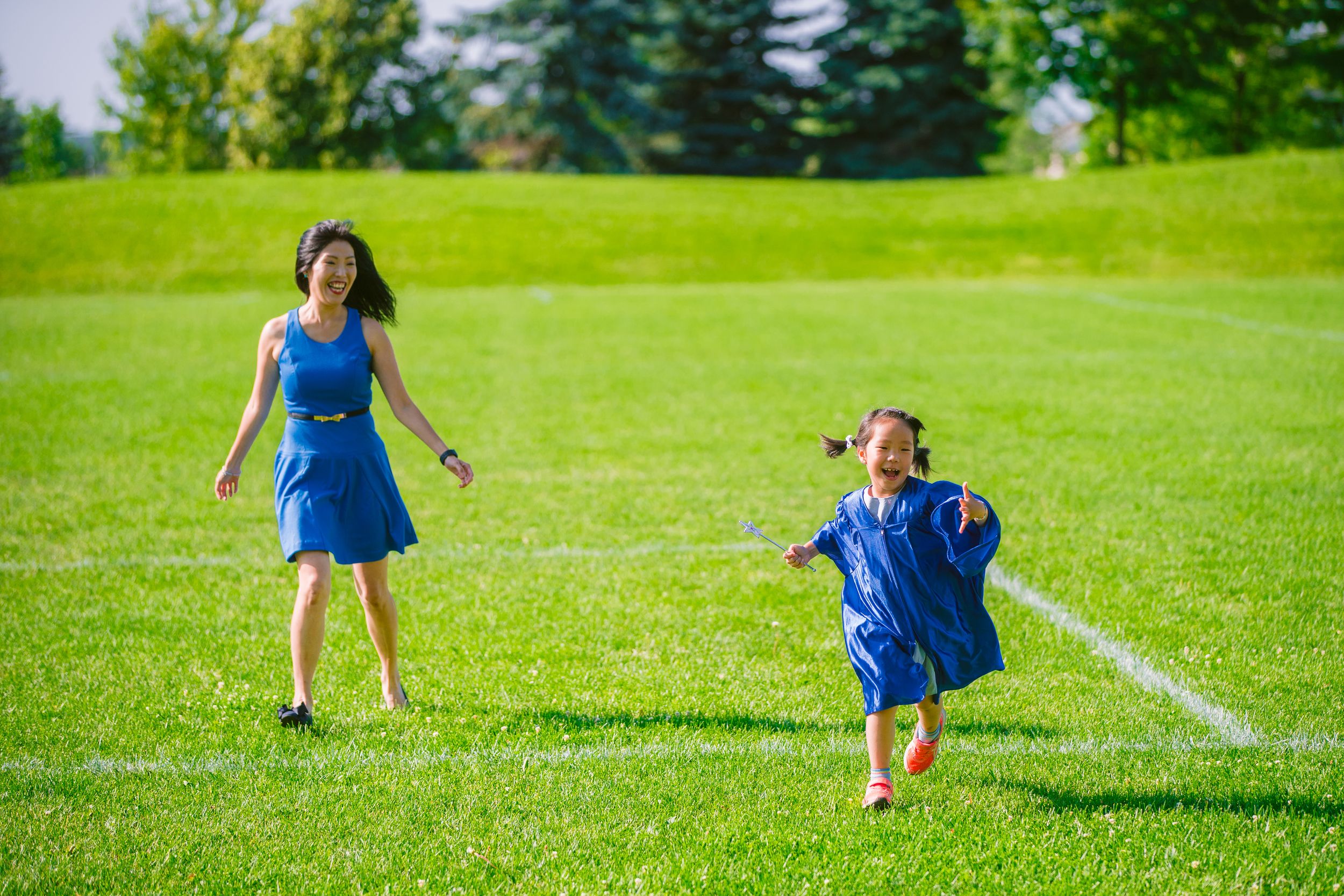Two people in matching blue dresses play and dance together on a sunny green lawn during summer.