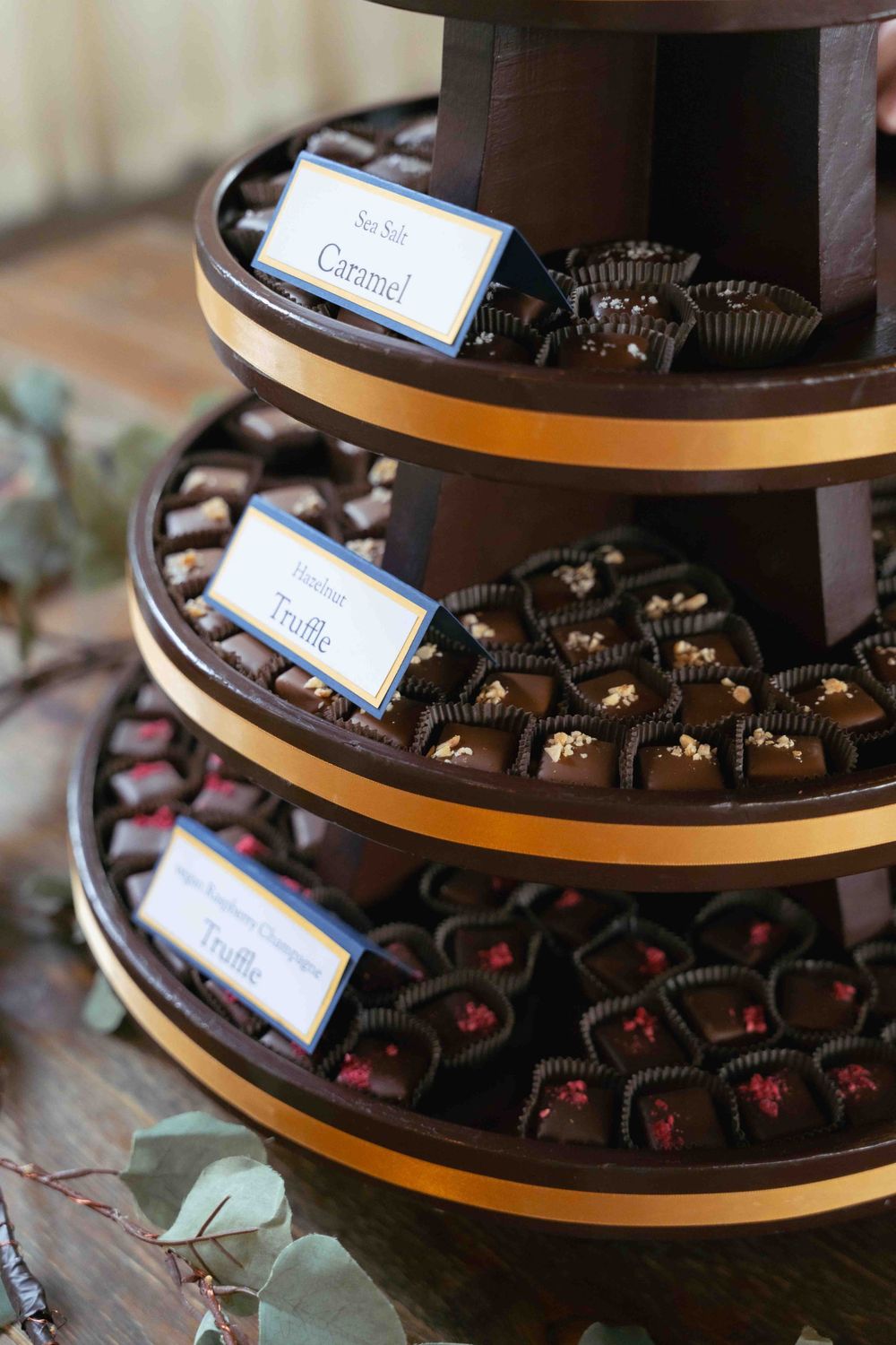 Three-tiered display of chocolate truffles with caramel and flavor labels at an event. At Fairlie, Chicago