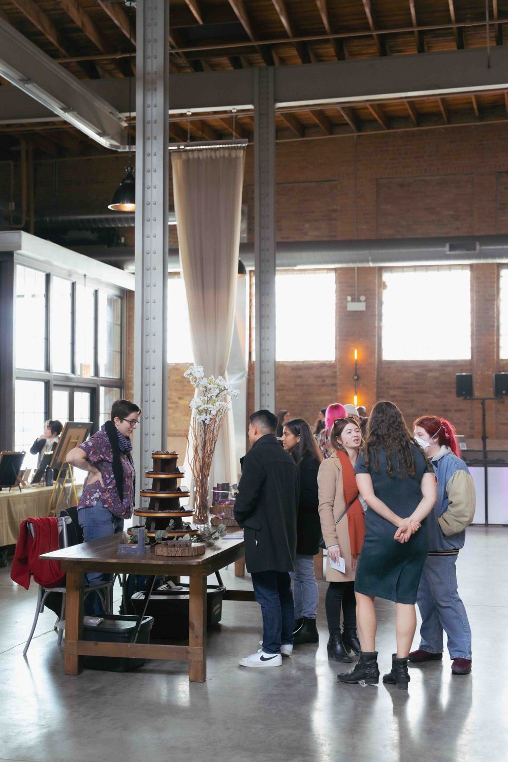 Industrial event space with exposed brick walls and guests gathering near display tables. At Fairlie, Chicago