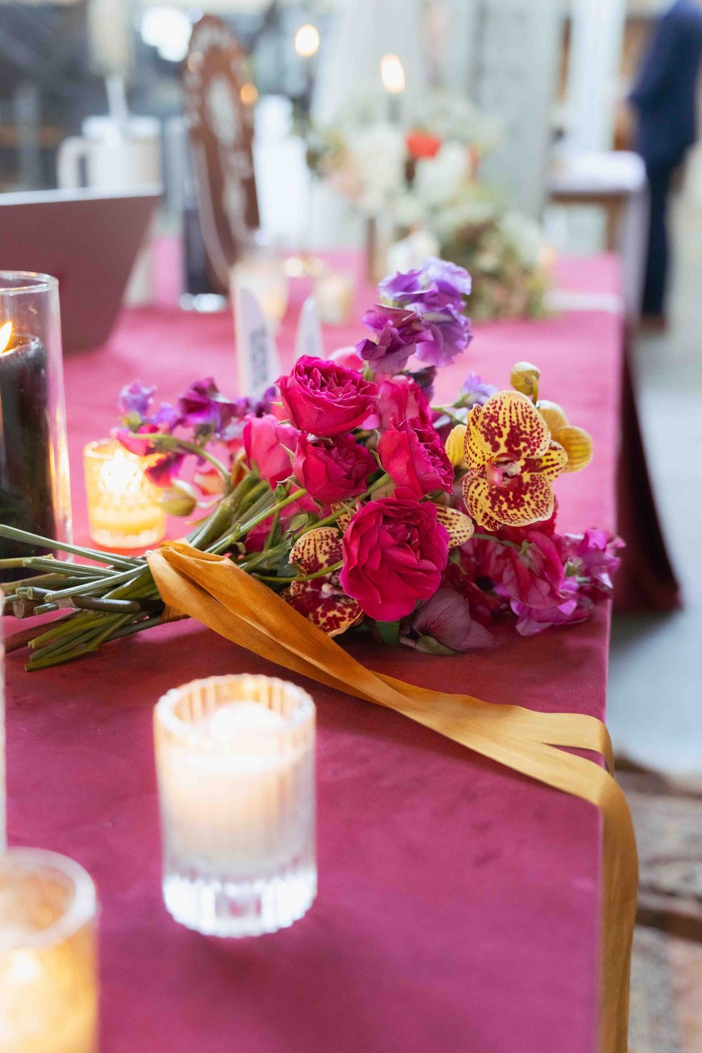 Floral arrangement with roses and orchids alongside glowing votives on burgundy table. At Fairlie, Chicago