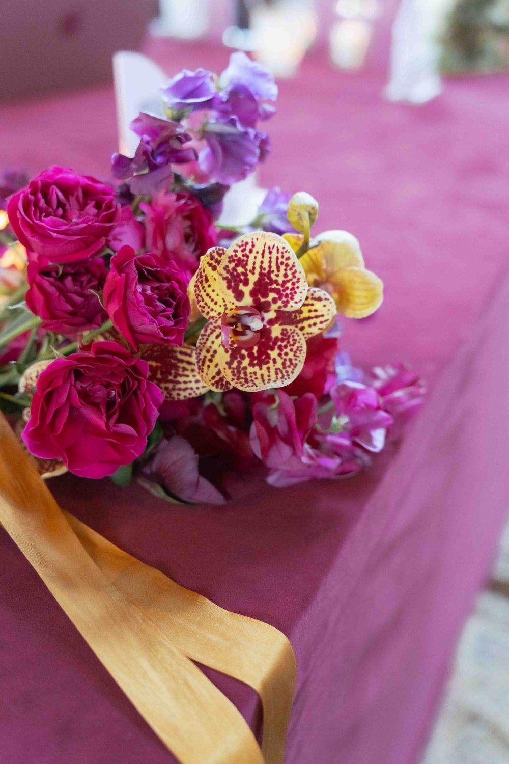 Close-up of deep pink roses and golden orchids against burgundy tablecloth. By FORGET ME NOT ARTS