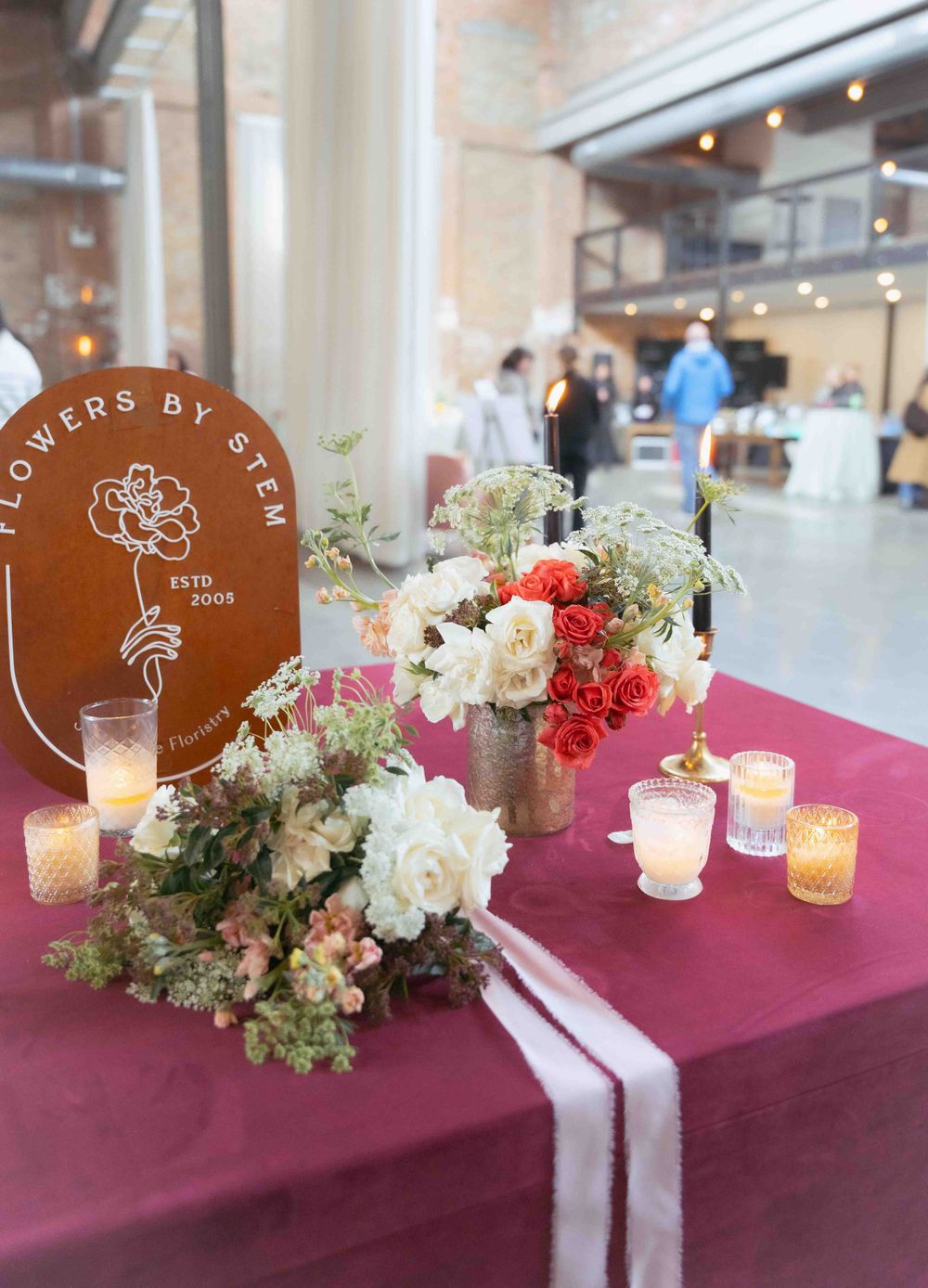Floral decorations and candles at an event with 'Flowers by Sara' sign visible.