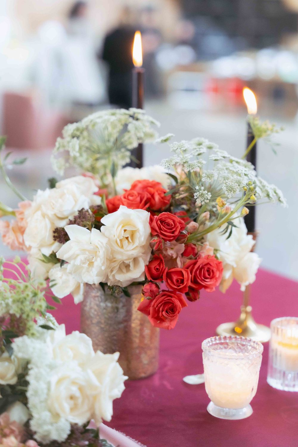 Elegant floral arrangement with white and coral roses alongside lit candles on burgundy tablecloth. By FORGET ME NOT ARTS