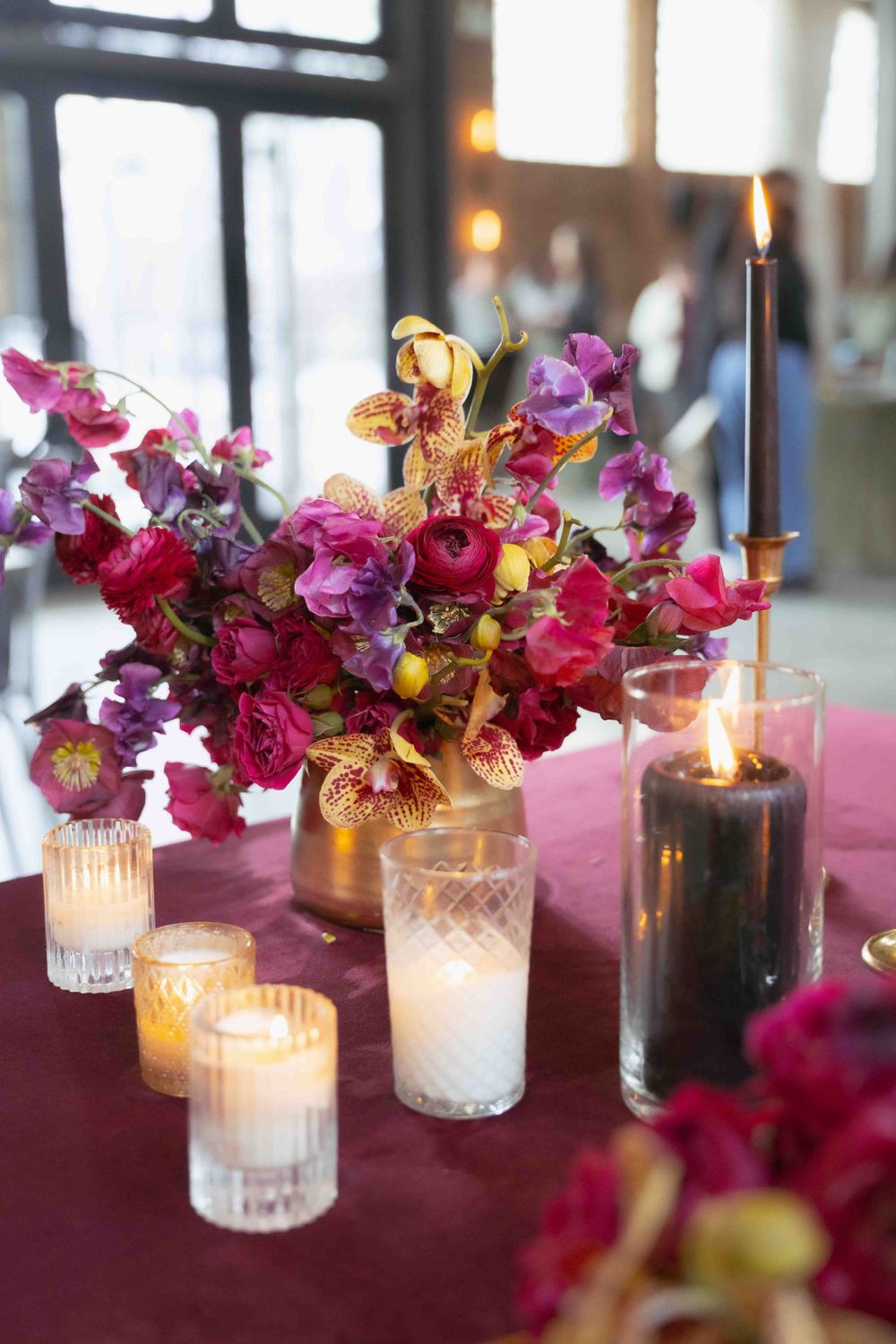 Vibrant pink and orange floral centerpiece with glowing candles on burgundy tablecloth. By FORGET ME NOT ARTS