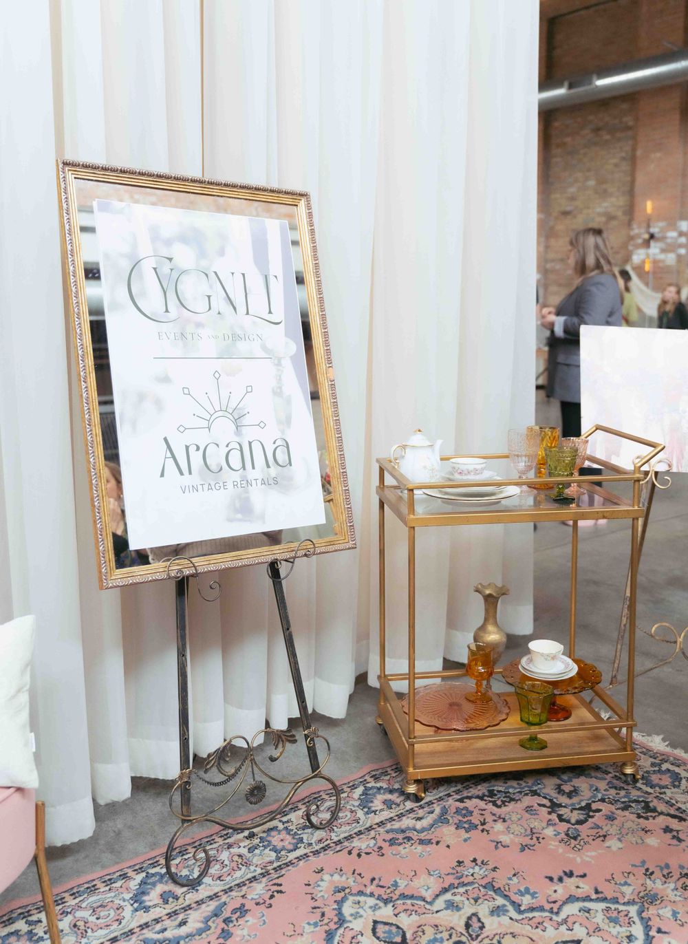 Elegant event signage for 'Cigall and Arcana' displayed on easel next to gold bar cart. By FORGET ME NOT ARTS