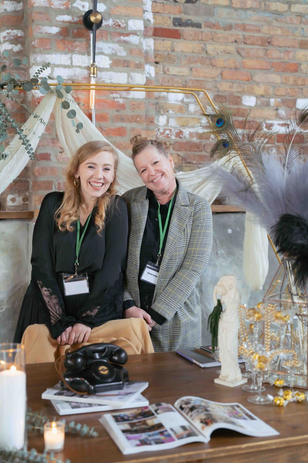Two event staff members posing at a decorated display table with vintage props and printed materials. At Fairlie, Chicago