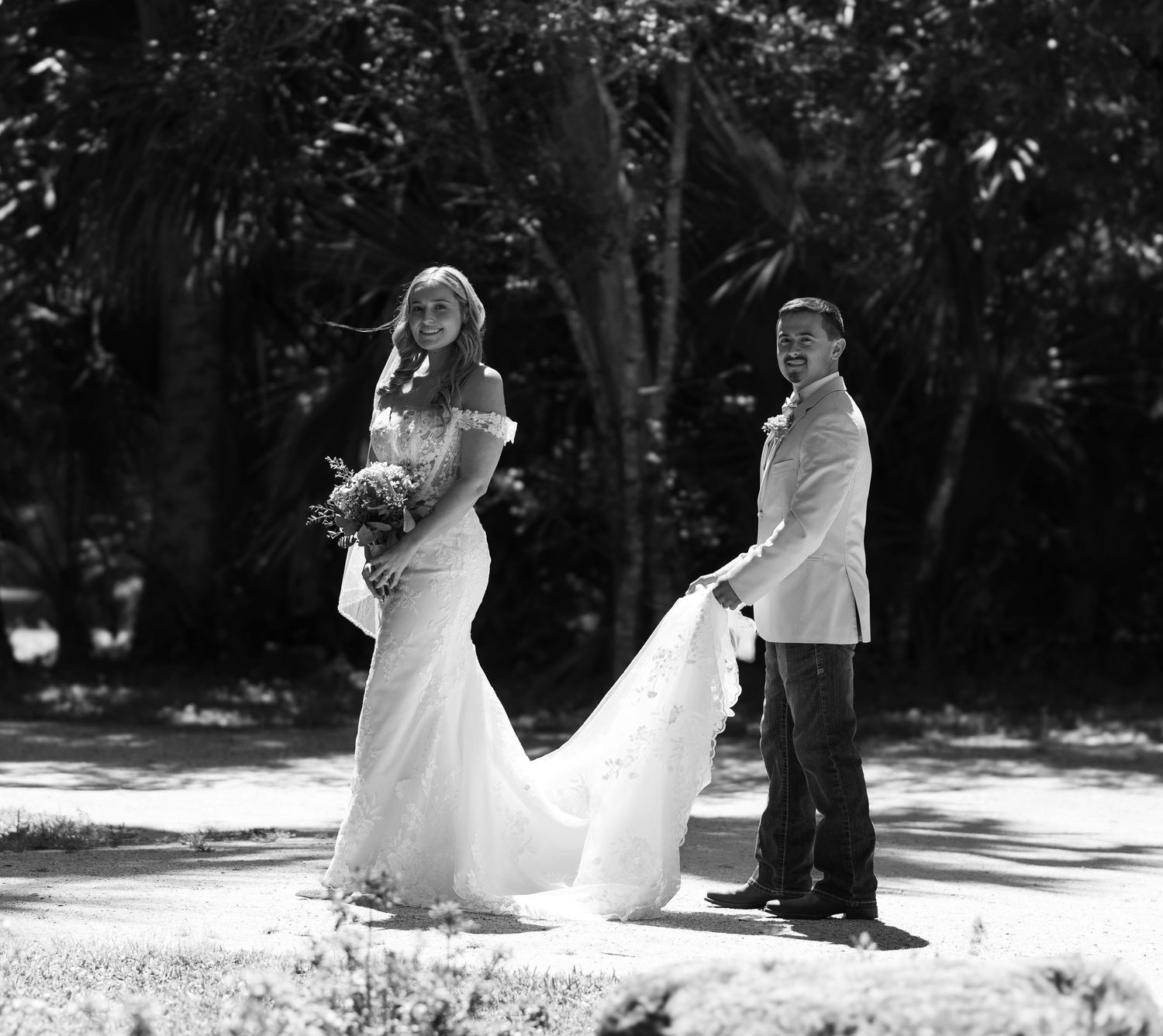 A black and white wedding photo captures playful moment with bride's dress flowing in the wind.