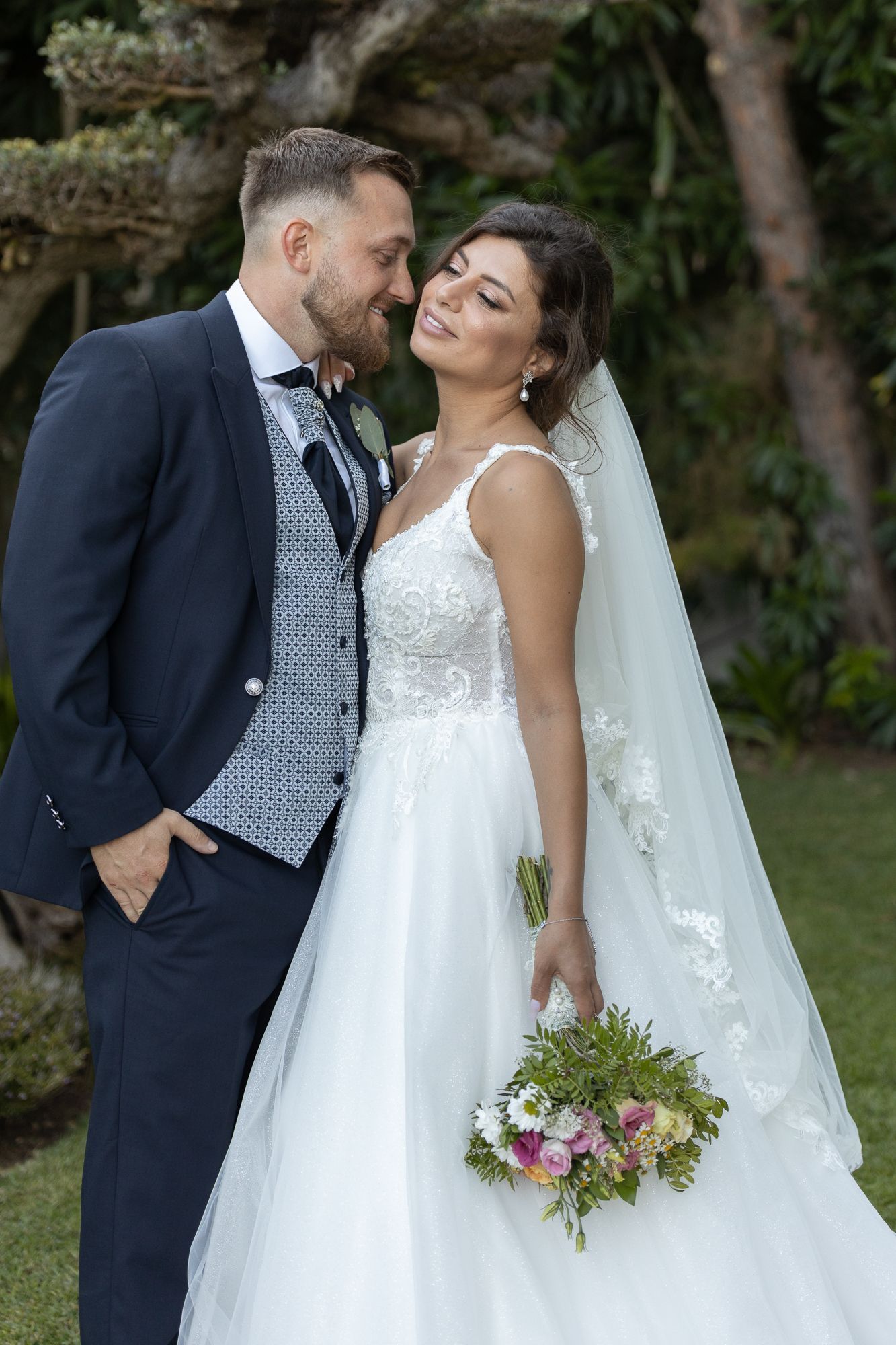 Wedding couple sharing intimate moment in garden setting with floral bouquet.
