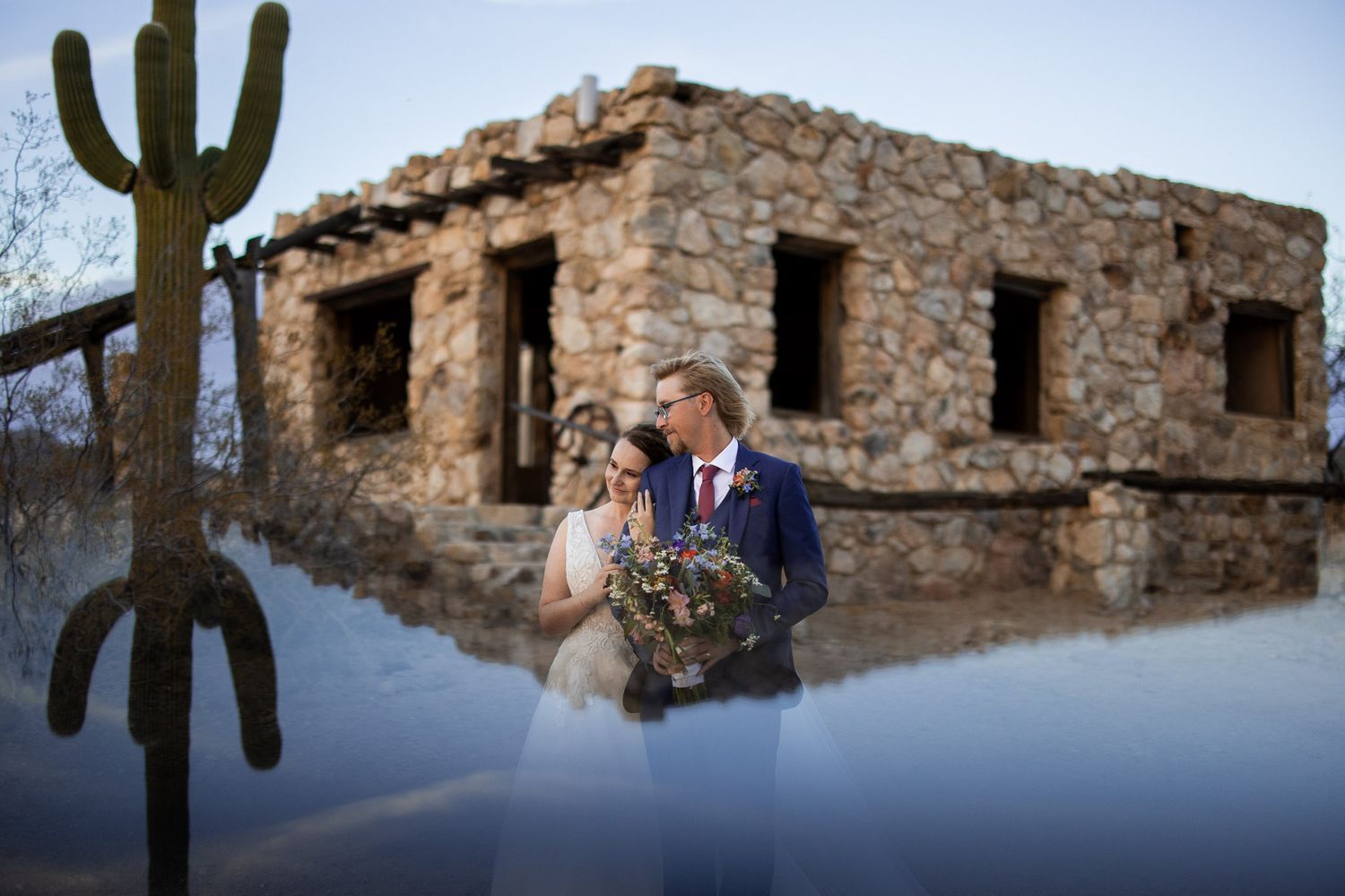 Rustic stone ruins and tall saguaro cactus frame a romantic scene in the Arizona desert at sunset.