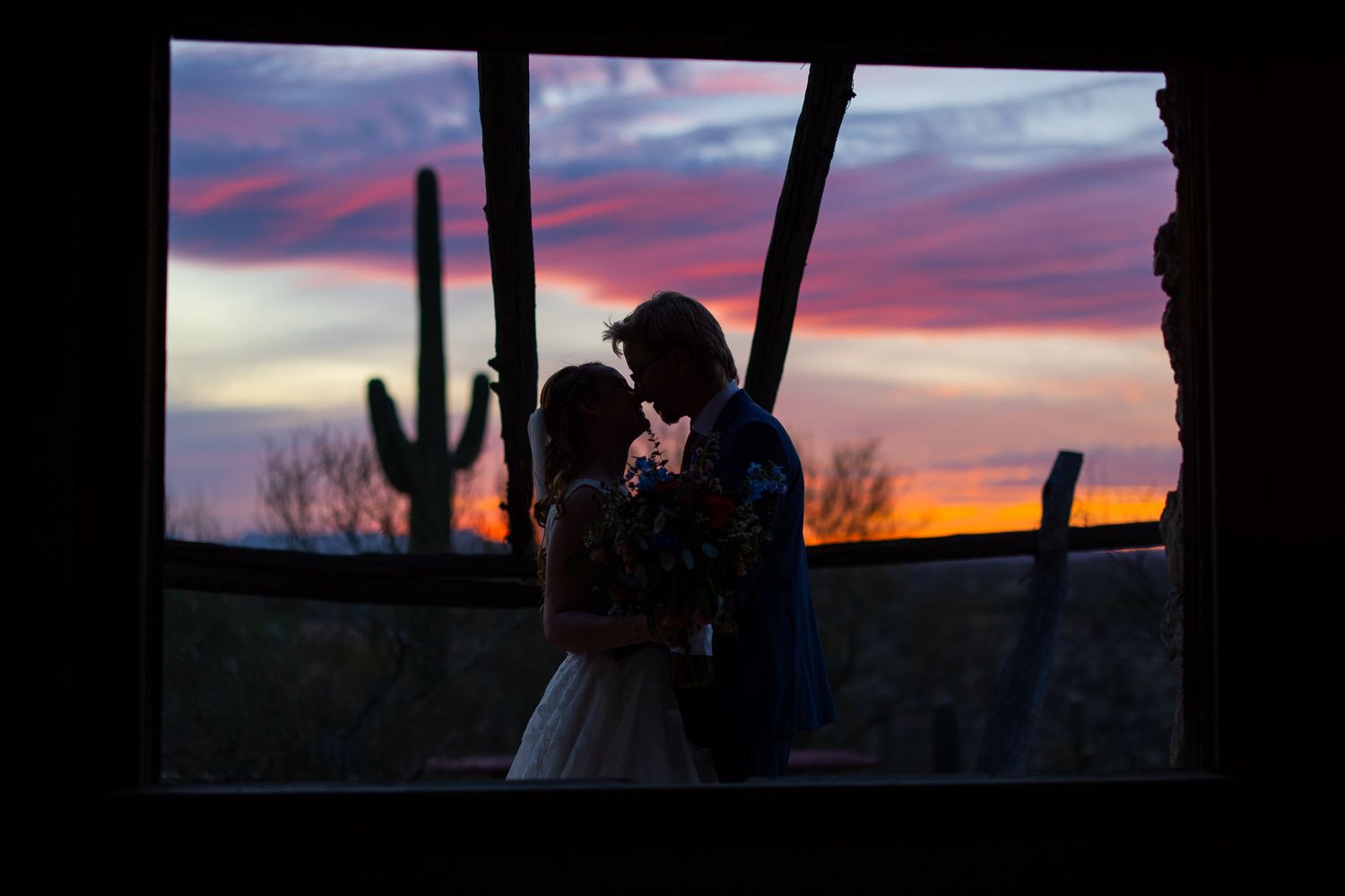 A romantic silhouette against a colorful desert sunset with saguaro cactus in the background.