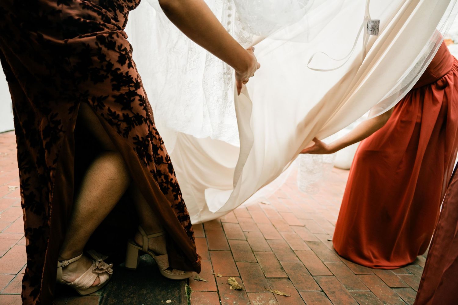 Close-up of flowing wedding dress and bridesmaid dresses on brick patio.