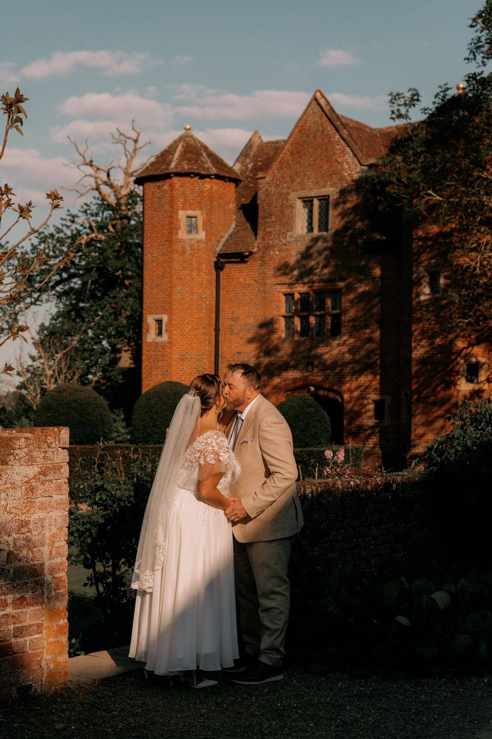 A romantic sunset moment with a couple embracing in front of a historic red brick castle with turrets.