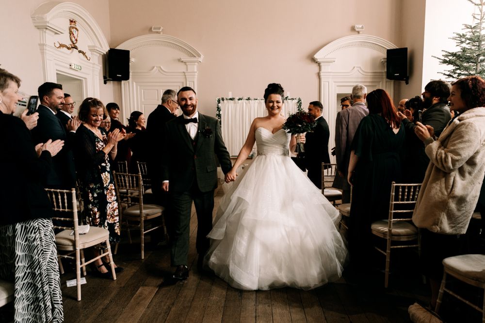 Guests celebrating and applauding during a grand entrance at an elegant indoor wedding ceremony.