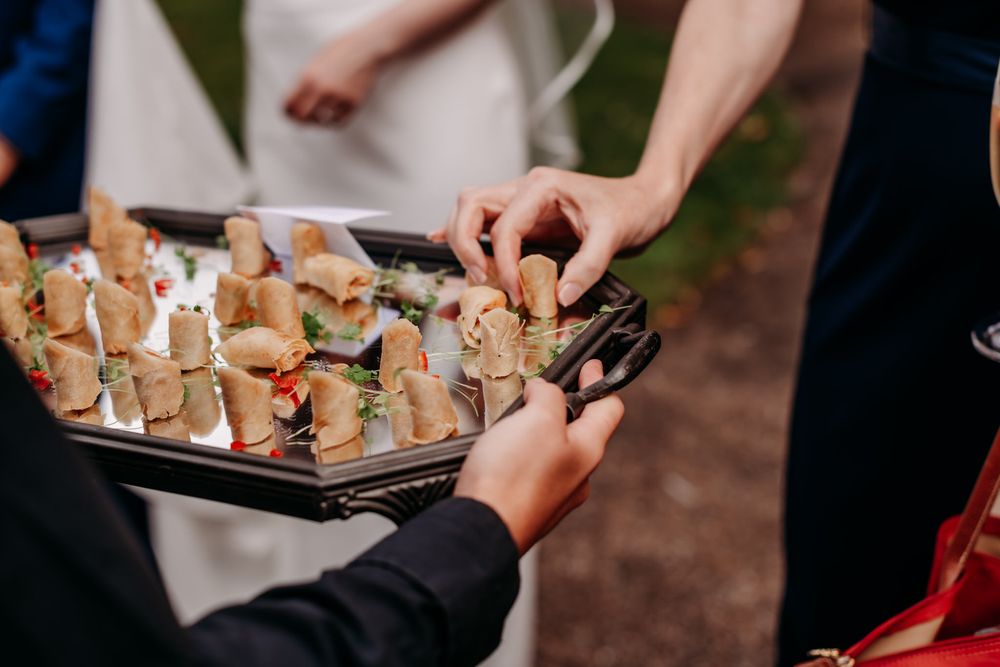 Hands serving appetizers and finger foods on a decorative platter at an elegant event.