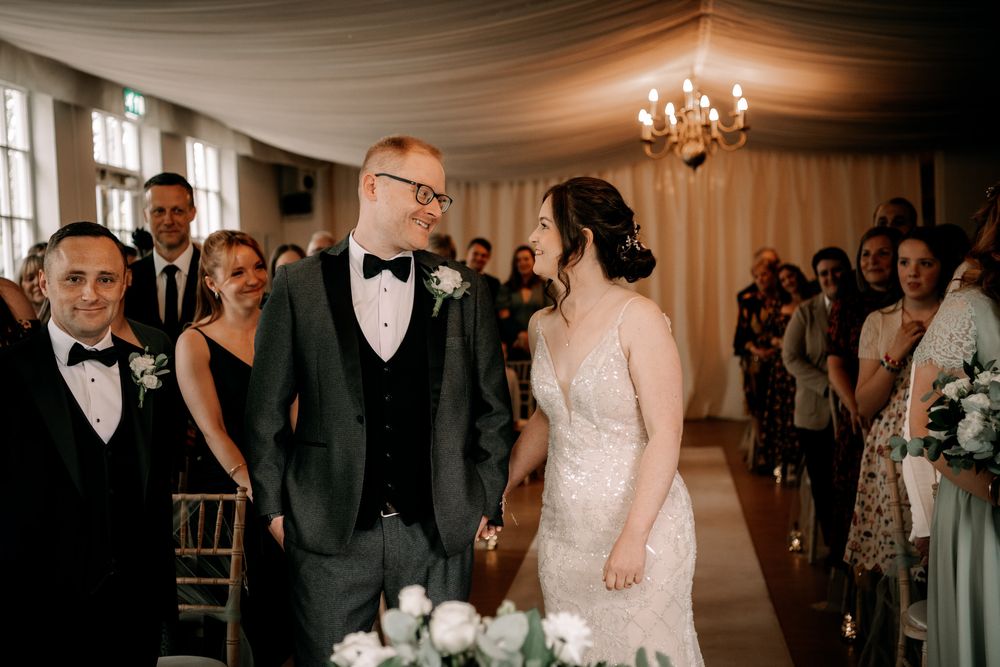 Wedding couple shares a loving moment while guests look on in an elegant reception hall with chandeliers.