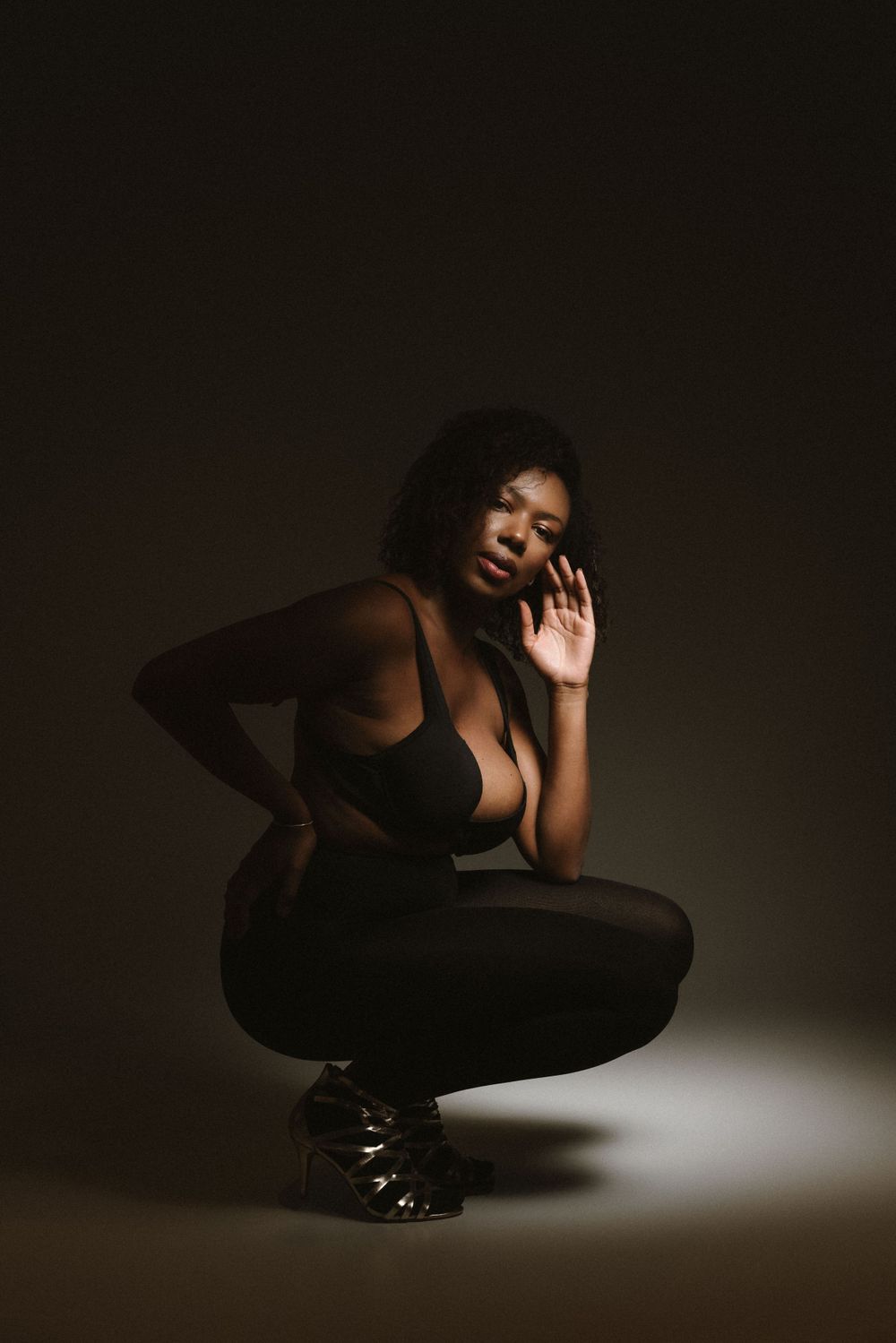 Artistic low-light portrait of person in black outfit crouching with dramatic pose.