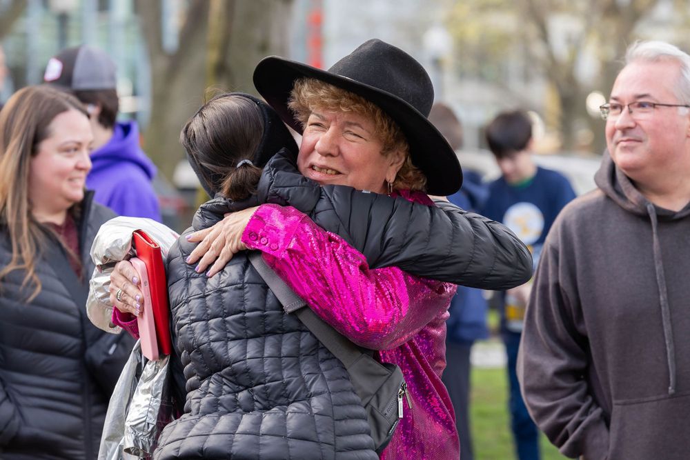 People sharing warm hugs at a community gathering in a park setting.