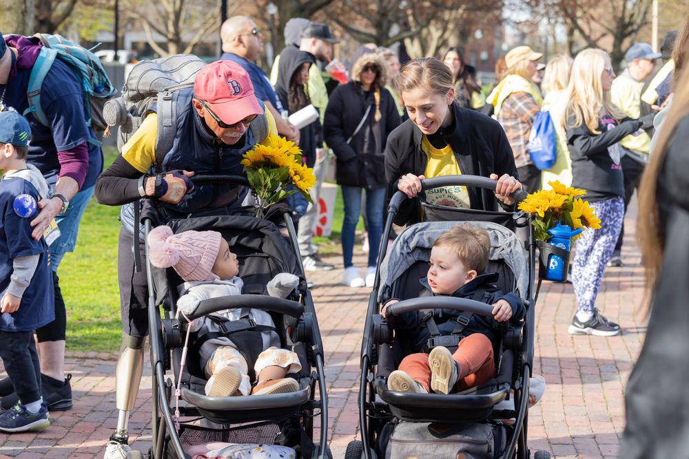 Children in strollers decorated with flowers participate in outdoor charity event.