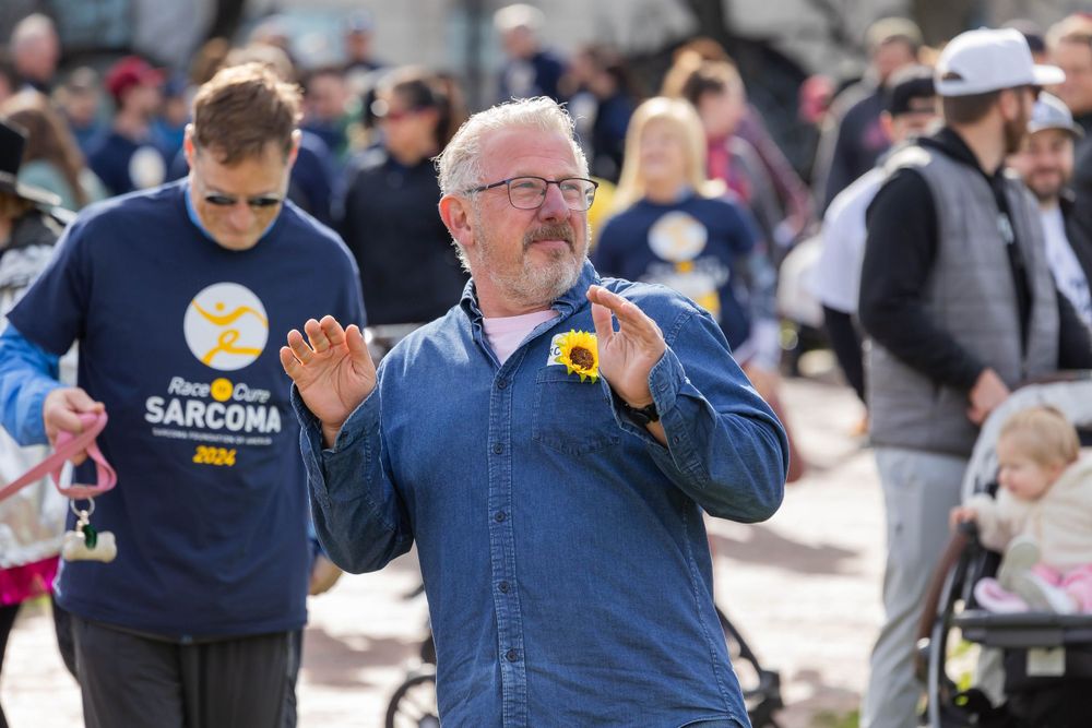 Man in navy jacket with yellow ribbon participates in outdoor charity walk.
