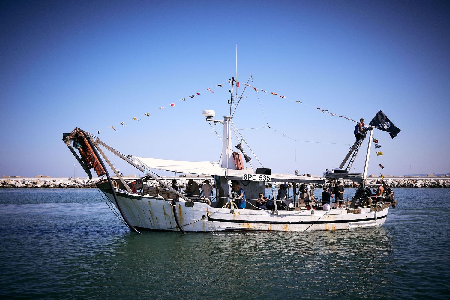 A decorated fishing boat with flags and banners sailing in calm waters.