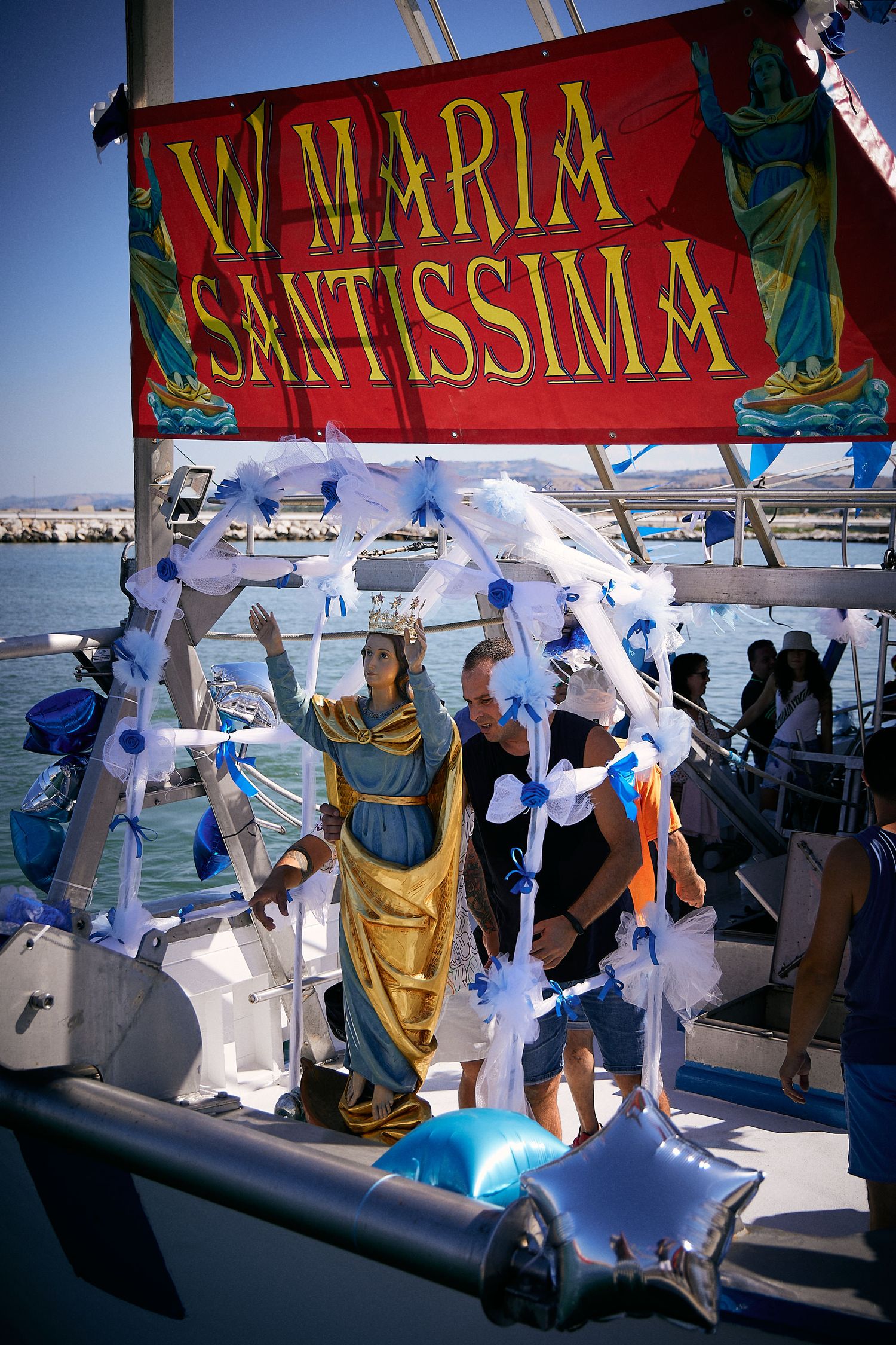A red banner reading 'W MARIA SANTISSIMA' displayed on a decorated boat with religious statues.