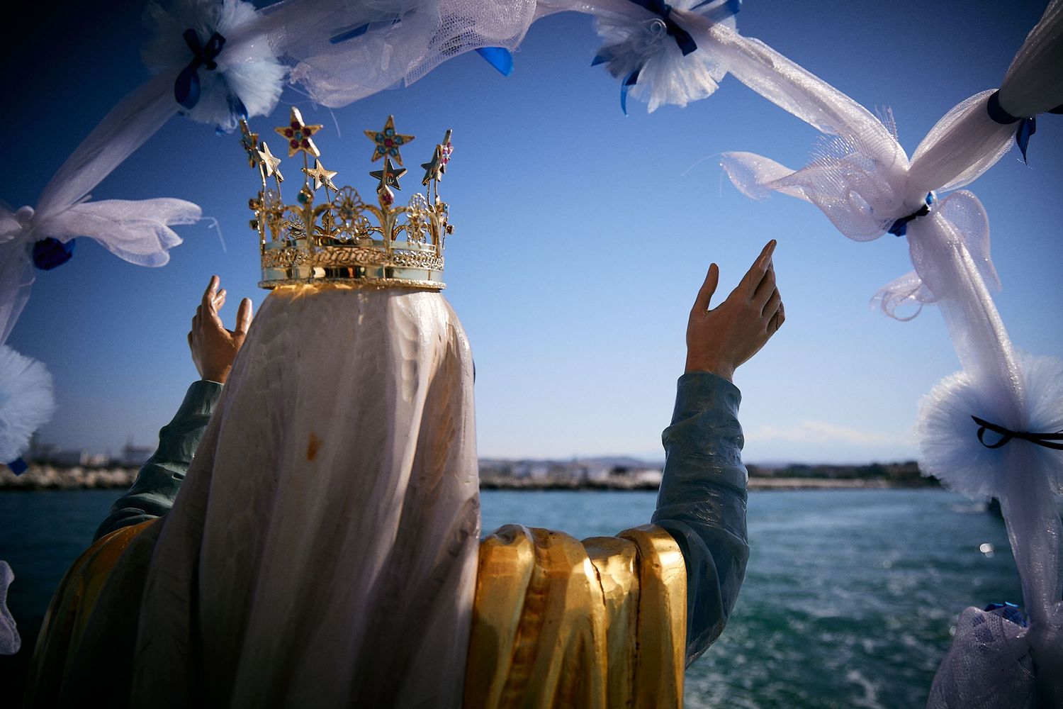 Figure wearing golden crown raises arms toward white doves against blue ocean backdrop.