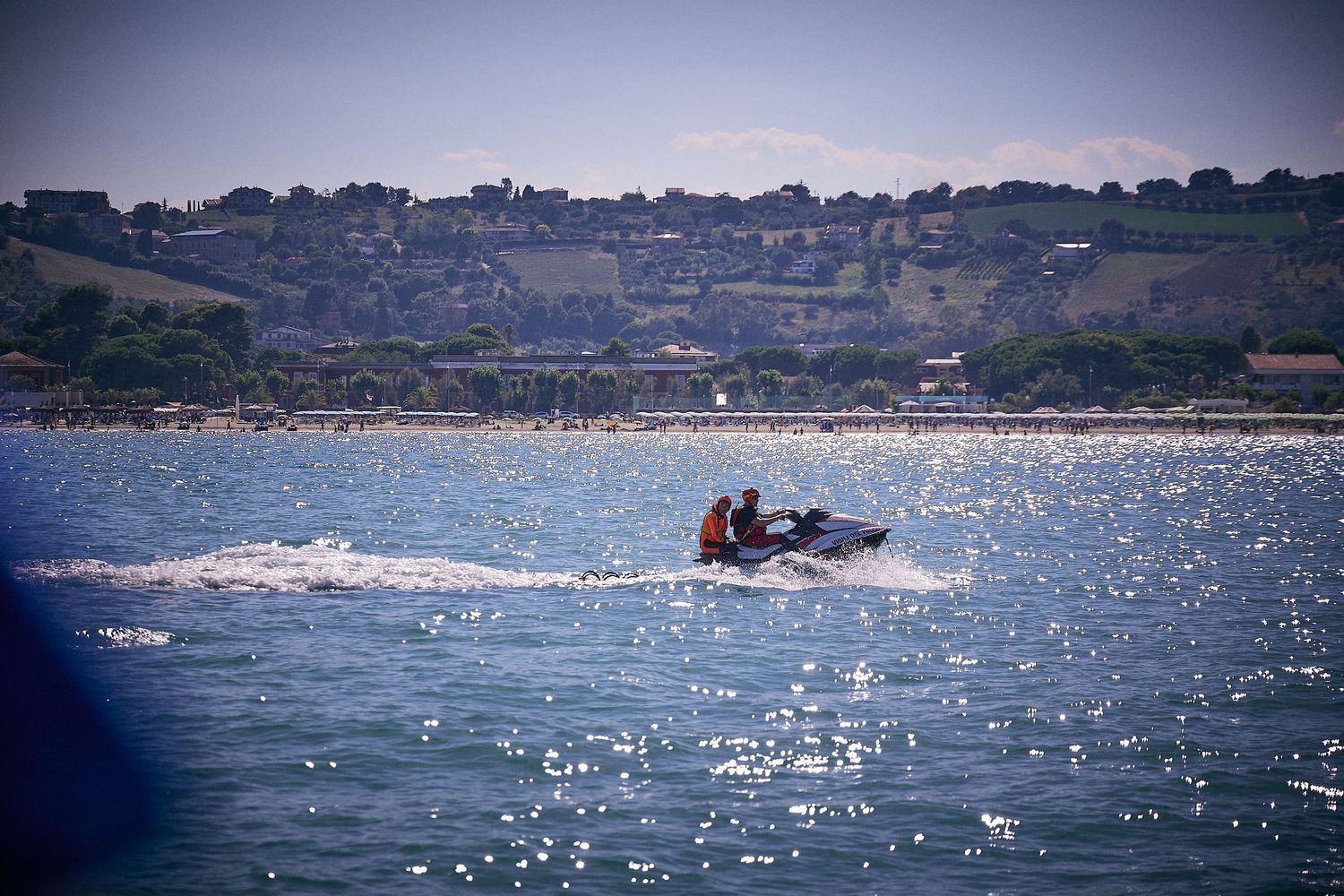Jet ski sprays water across sparkling bay with coastal homes in background.