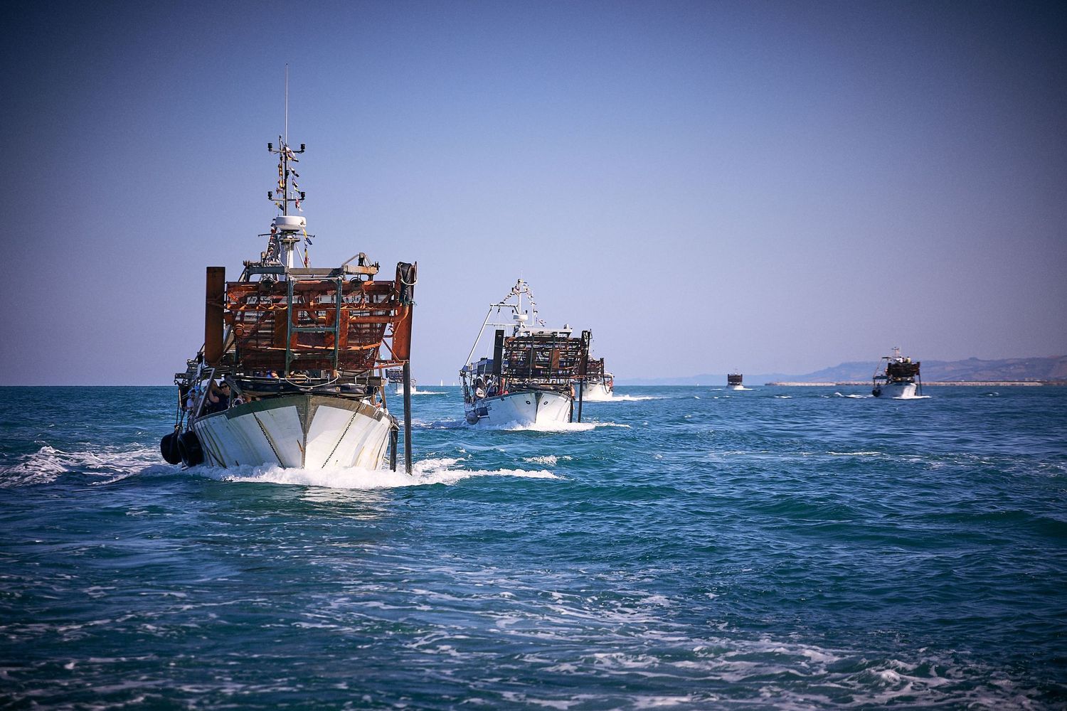 Three fishing boats cruise through blue ocean waters under clear sky.