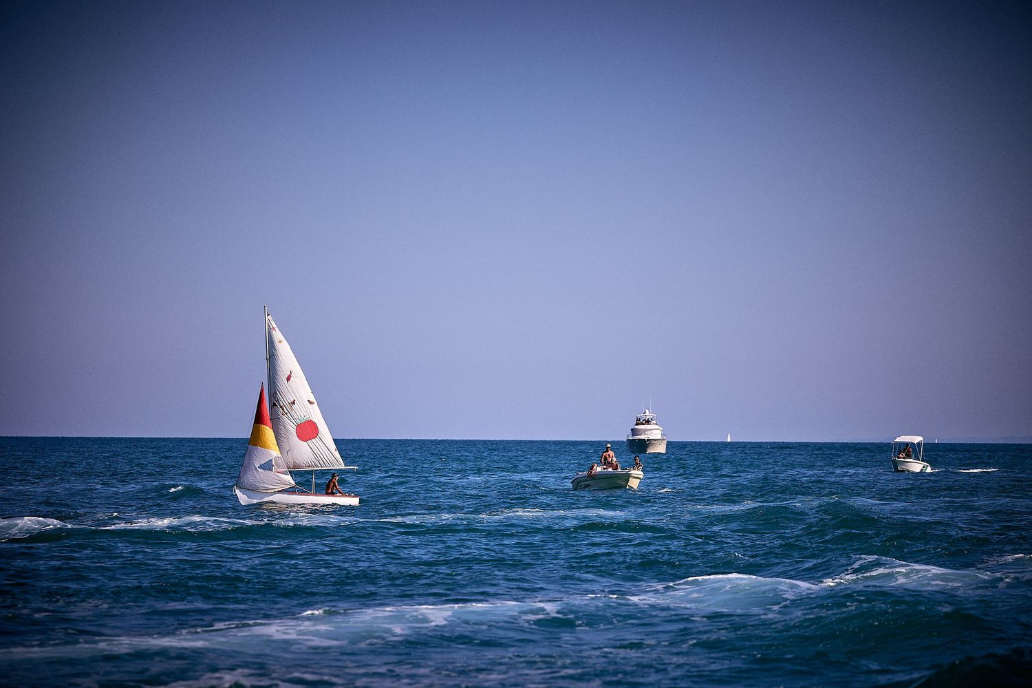 White sailboat and boats navigate blue waters on sunny day.