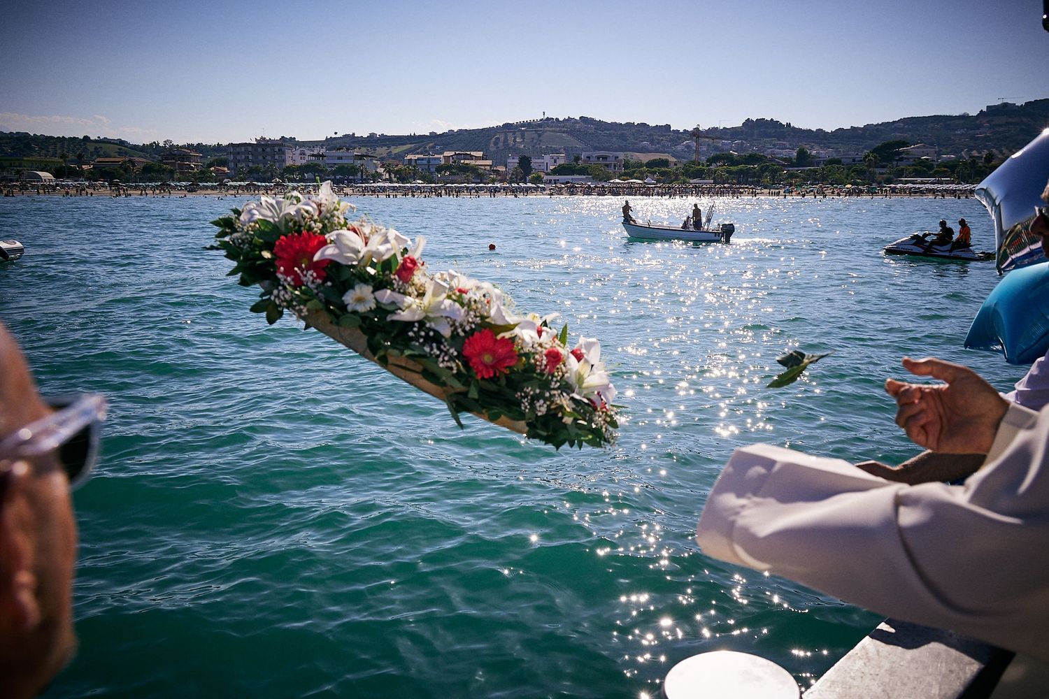 Colorful flower wreath being placed into sparkling blue ocean waters.