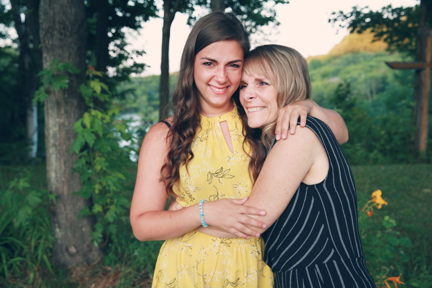 Two friends share a joyful embrace while wearing summer dresses outdoors.