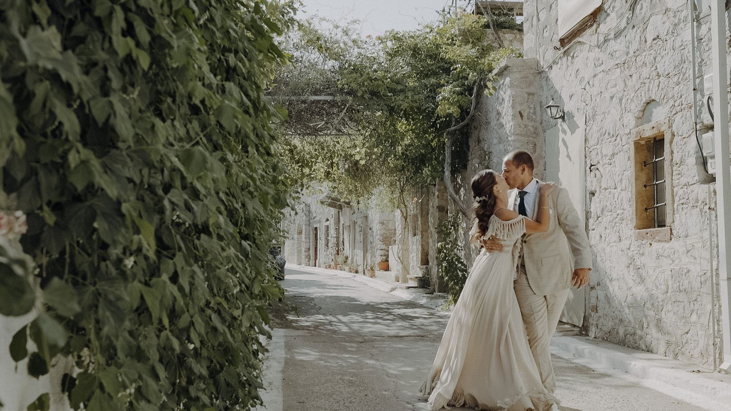 Romantic wedding moment in a charming stone-walled alley with climbing vines.