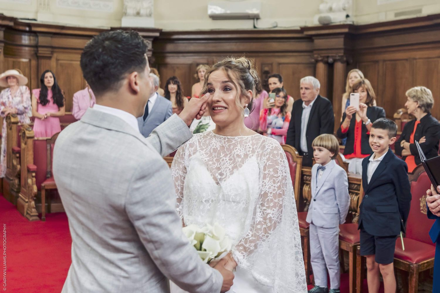 A wedding ceremony takes place in a historic room with red carpeting and wooden paneling.