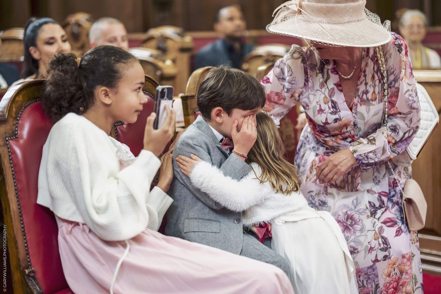 Several children laugh together while sitting in formal attire during what appears to be a wedding ceremony.