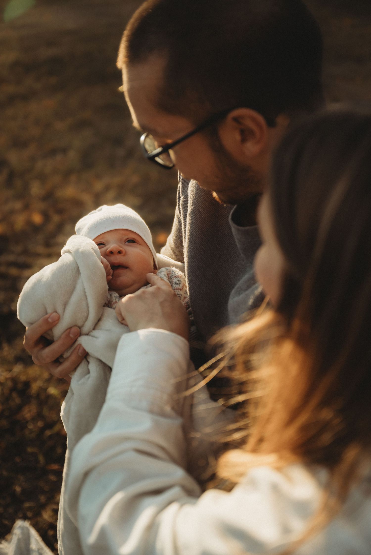 Family shares intimate moment with newborn baby during outdoor autumn photoshoot.